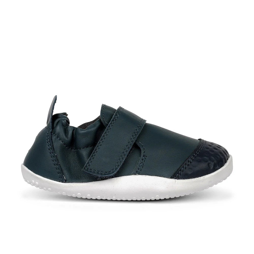 Calçado respeitador Bobux Xplore Navy para bebé, vista lateral, com sola branca flexível e fecho de velcro.