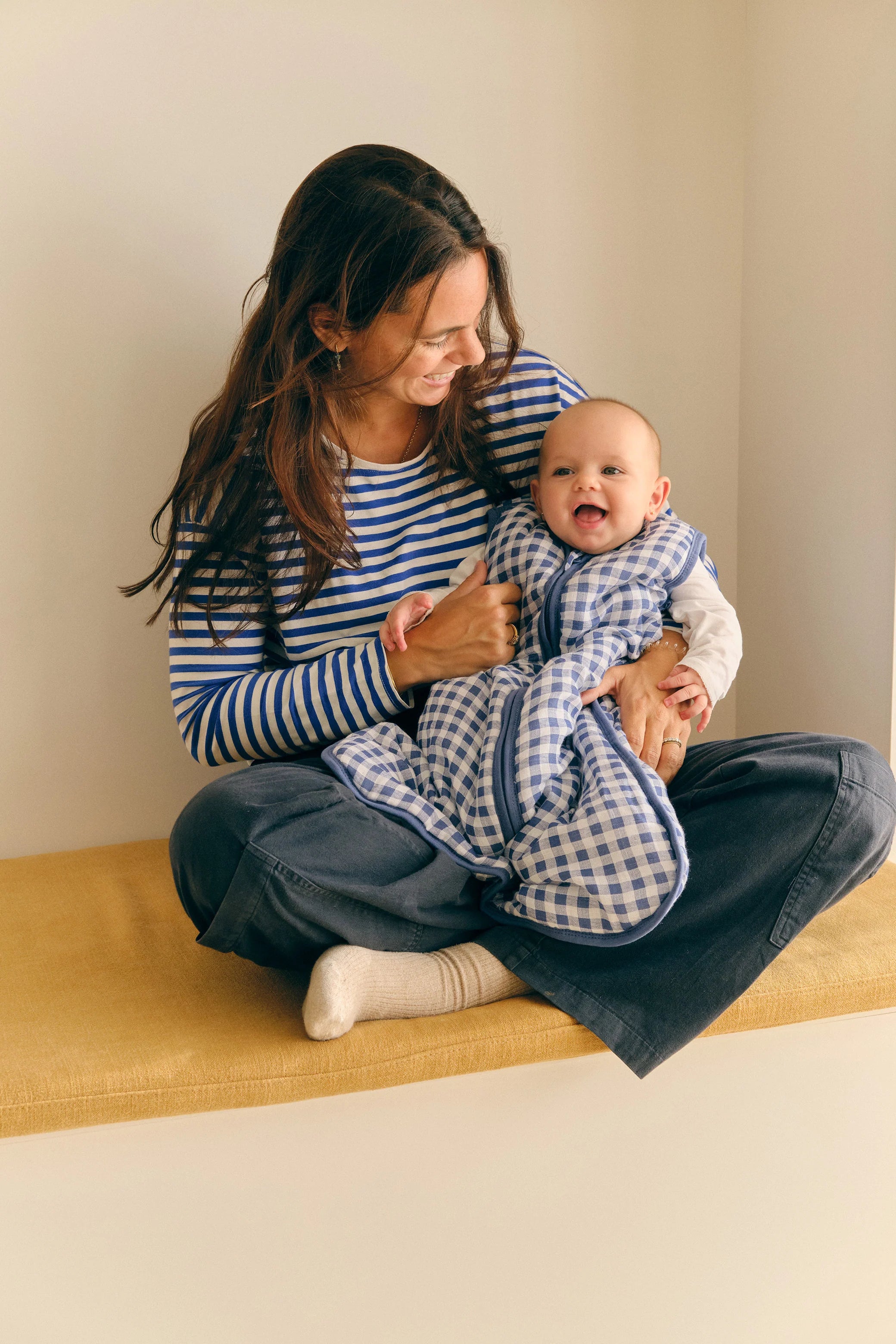 Bebé sorridente dentro do saco de dormir MolisandCo TOG 2.5, ao colo de uma mãe, ambos em ambiente acolhedor.