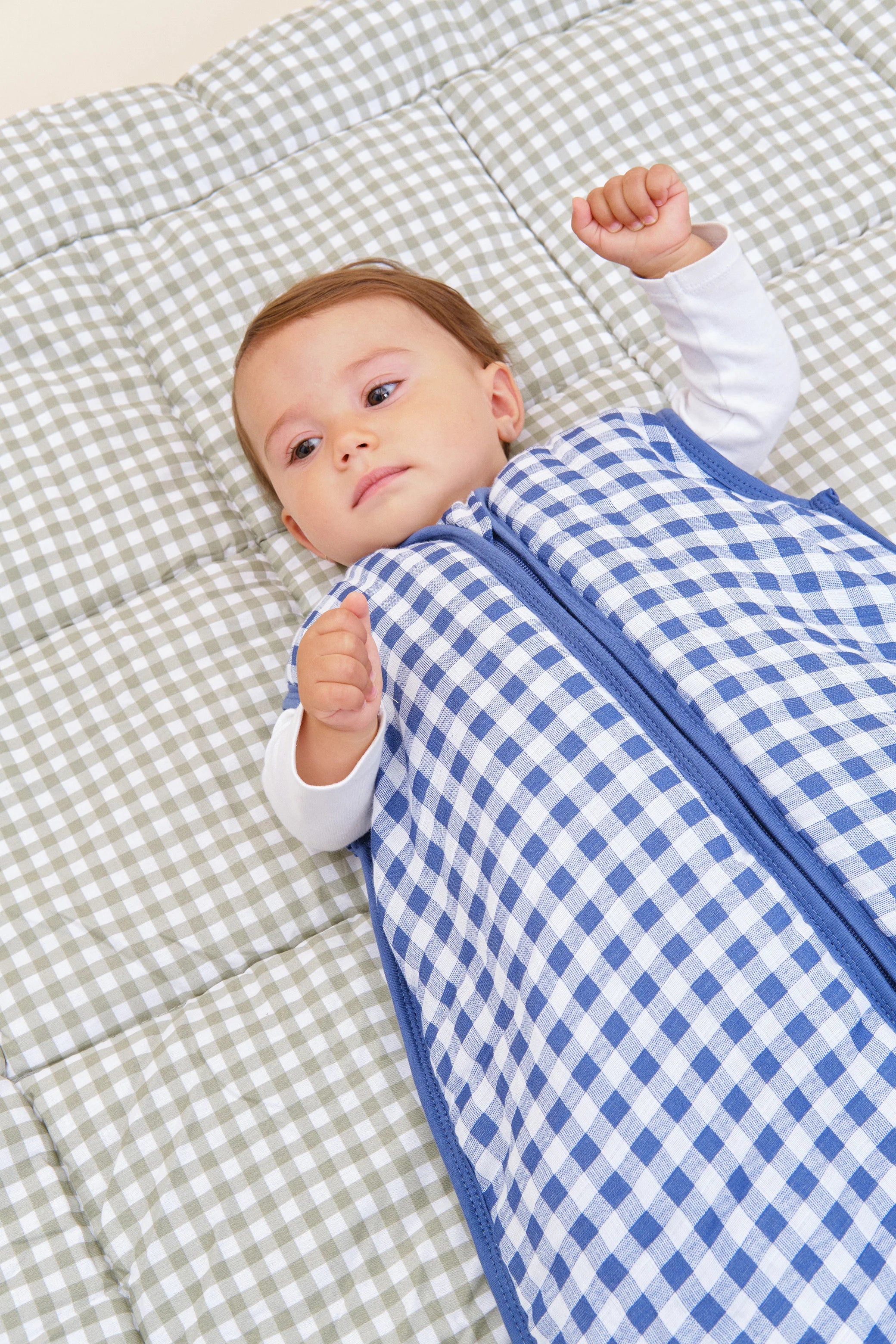 Bebé deitado de costas, vestido com o saco de dormir MolisandCo TOG 2.5 azul e branco, sobre um cobertor.