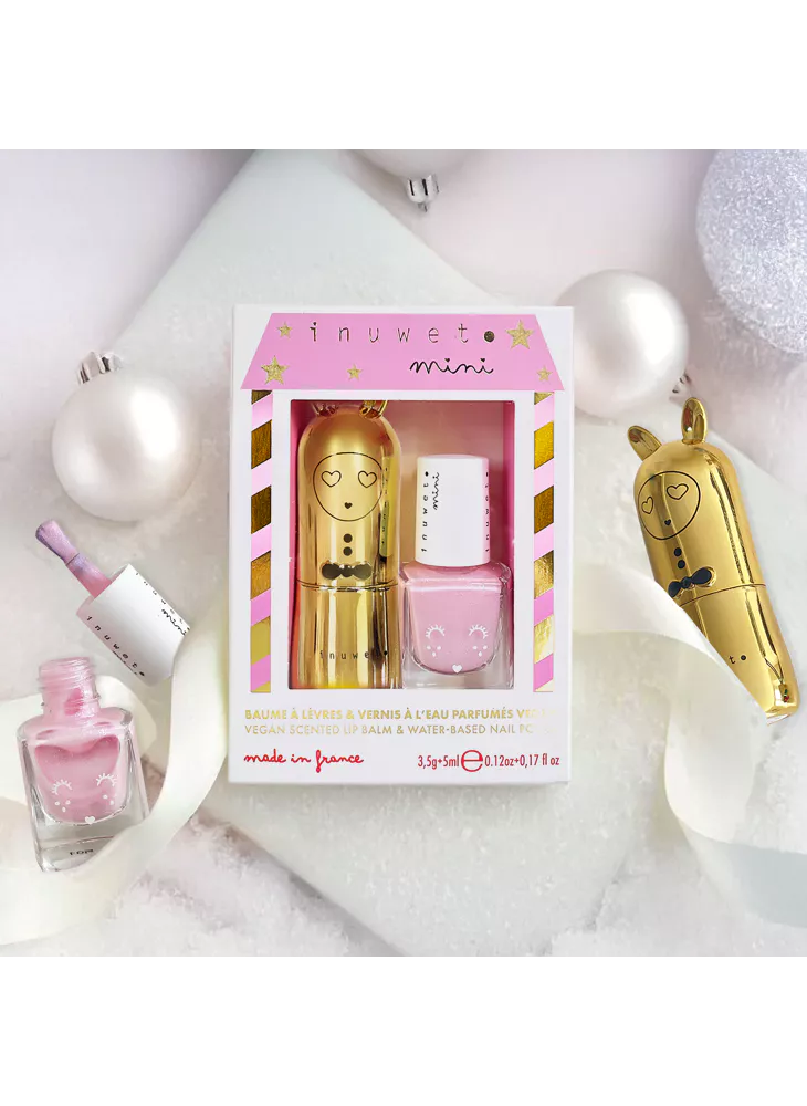 Conjunto Inuwet de bálsamo labial dourado e verniz rosa sobre fundo branco com decorações natalícias, pronto para presente.