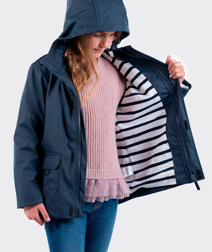 Criança a abrir o casaco impermeável Igor azul-marinho, revelando o interior forrado a riscas e uma camisola rosa.