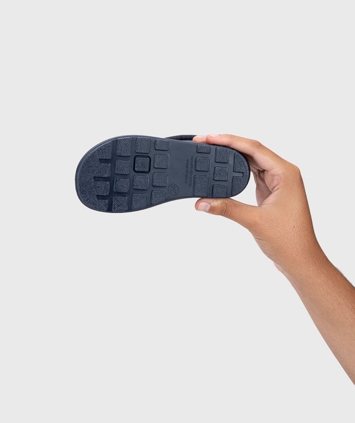 A sola antiderrapante de uma galocha Igor Yogi CUELLO MARINO azul, segurada por uma mão, mostrando o padrão de tração.