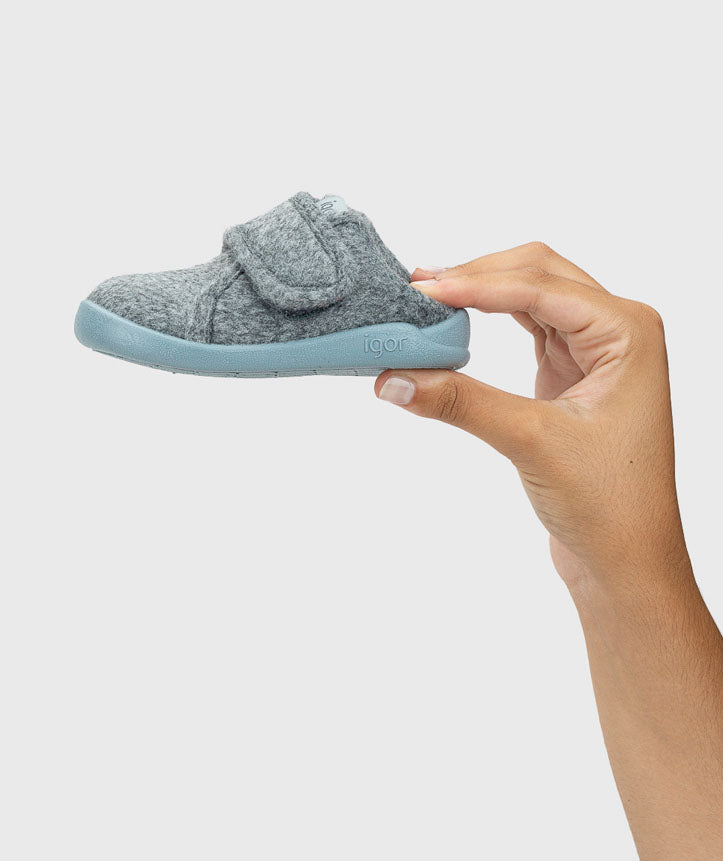 Uma mão segura uma pantufa Igor Homie cinzenta e azul-oceano, destacando o seu tamanho compacto e leveza.