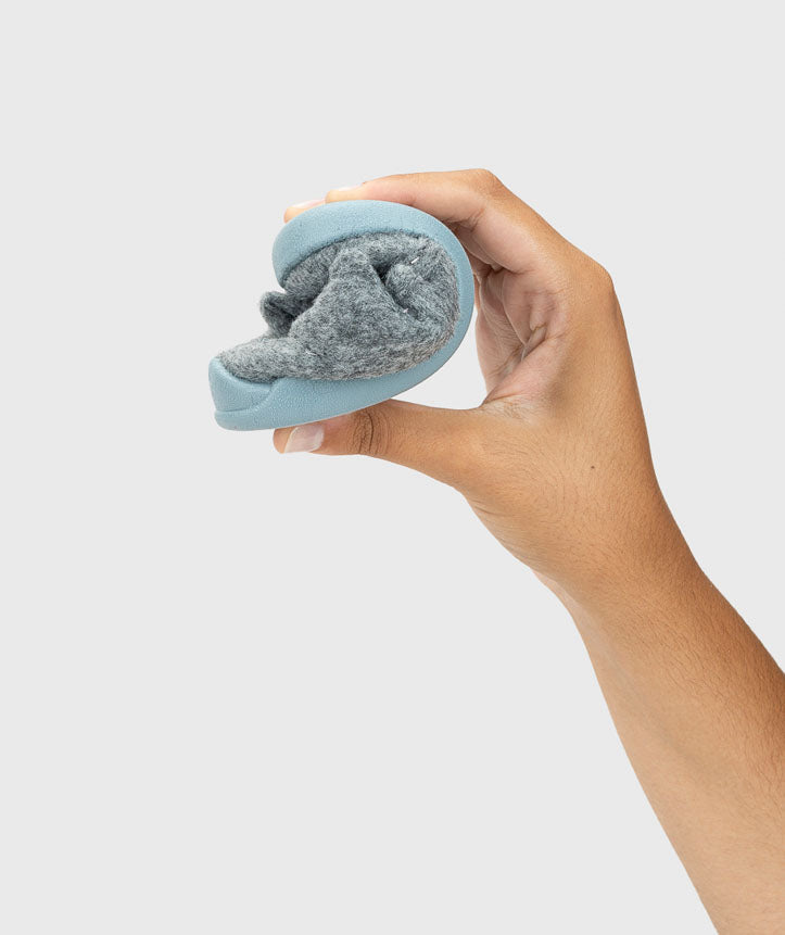 Uma mão dobra uma pantufa Igor Homie cinzenta e azul-oceano, demonstrando a extrema flexibilidade da sola.