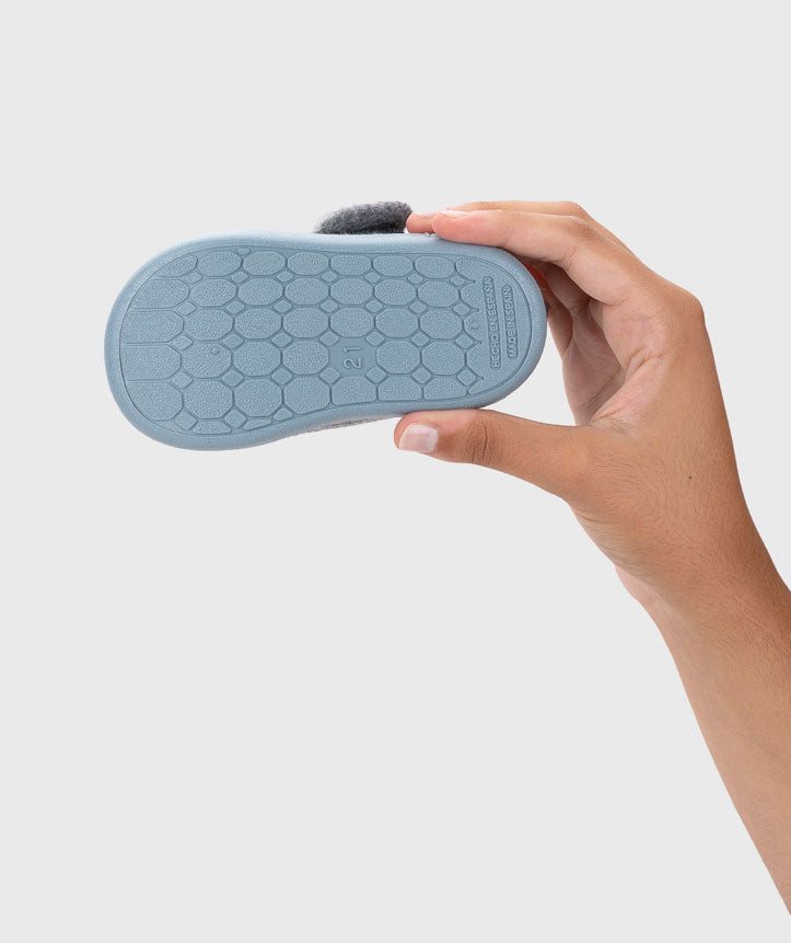 Uma mão segura a sola azul-oceano de uma pantufa Igor Homie, mostrando o padrão antiderrapante e a marca Igor.