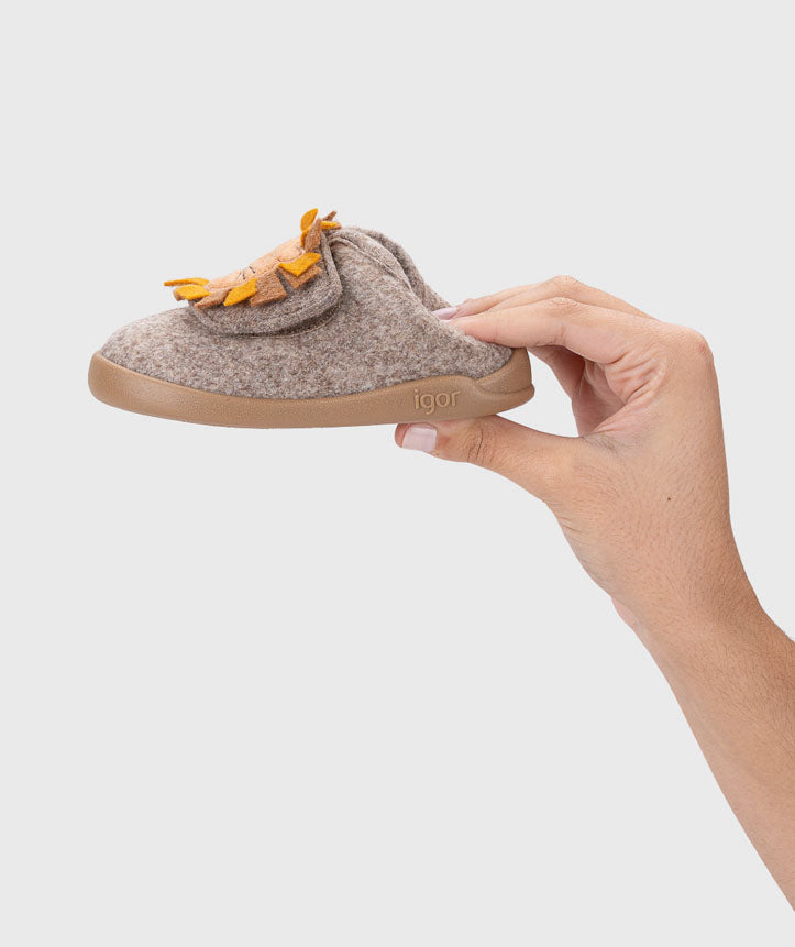 Mão a segurar uma pantufa Igor Barefoot HOMIE LEON TAUPE, destacando a leveza e o design lateral com leão.