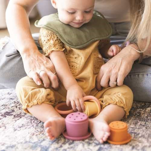 Bebé a brincar com os vasos de silicone Tiny Twinkle no chão, mostrando a interação com as texturas e cores.