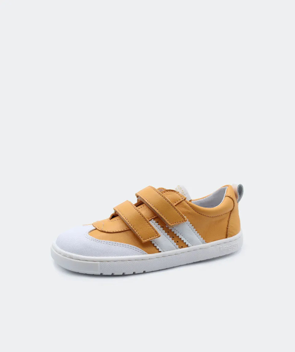 Vista lateral das sapatilhas Blanditos Marea Naranja (tom amarelo mostarda), calçado respeitador infantil com base branca, detalhes e velcro em amarelo mostarda e risca lateral branca. Calçado Barefoot.