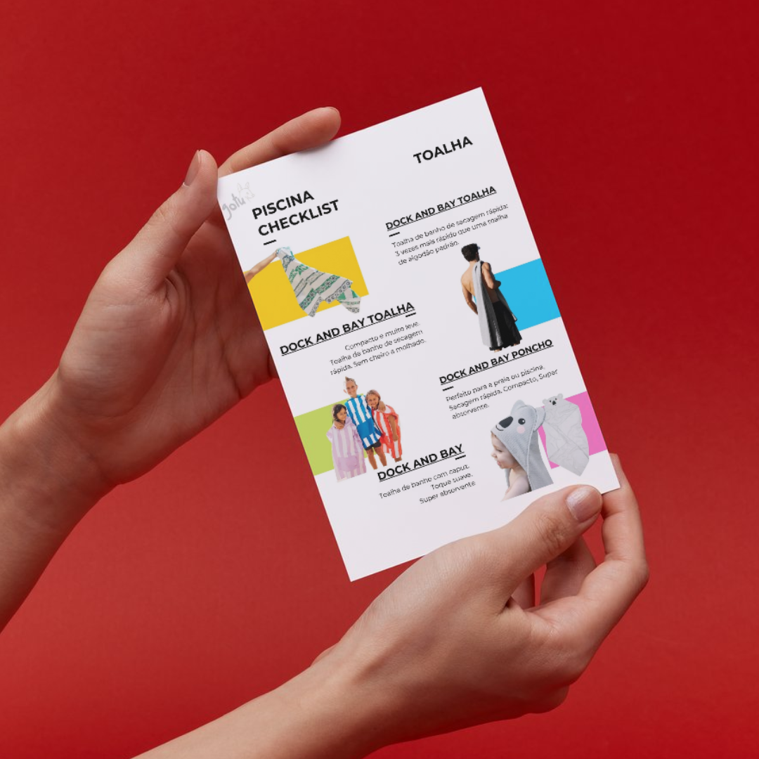 Mãos segurando a checklist impressa, mostrando a lista de itens para praia e piscina, incluindo toalhas Dock and Bay.