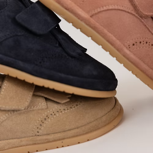 Detalhe de três sapatilhas Rutis - Carneiras PiuPiu em diferentes cores (areia, azul-escuro, rosa), empilhadas, mostrando a textura da camurça e a sola.