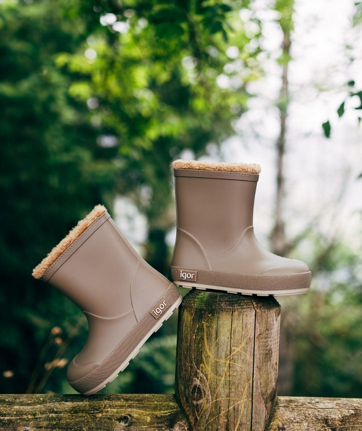 Galochas infantis em ambiente externo, pousadas sobre troncos de madeira, demonstrando a resistência e versatilidade para uso ao ar livre.