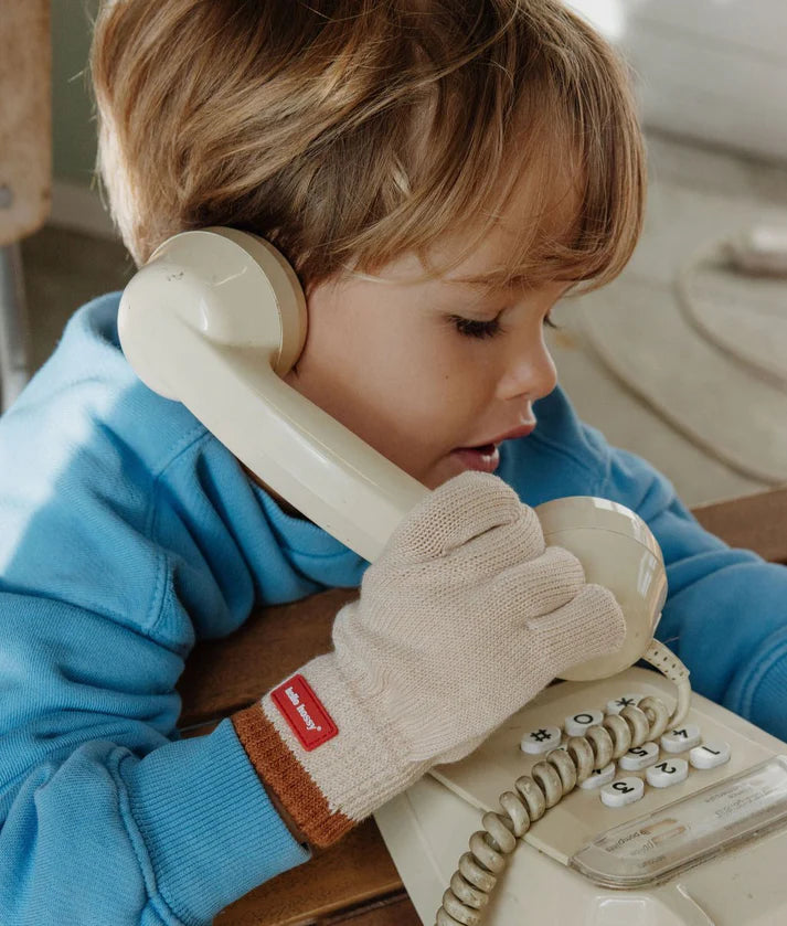 Menino com luvas HELLO HOSSY Handy Creamy cor creme e punho castanho, a brincar com um telefone antigo.