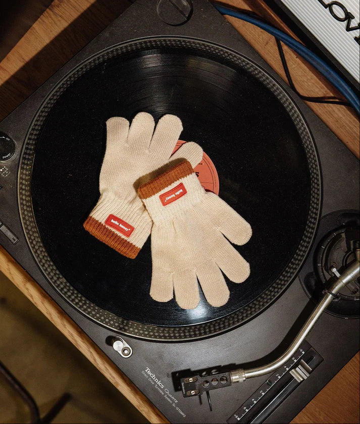 Par de luvas HELLO HOSSY Handy Creamy em malha creme com punhos castanhos, pousadas num gira-discos.