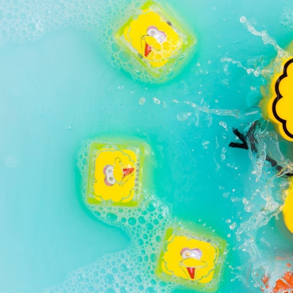 Três cubos de luz GloPals Poupas (Rua Sésamo) a brilhar na água azul com bolhas, mostrando o brinquedo em uso.