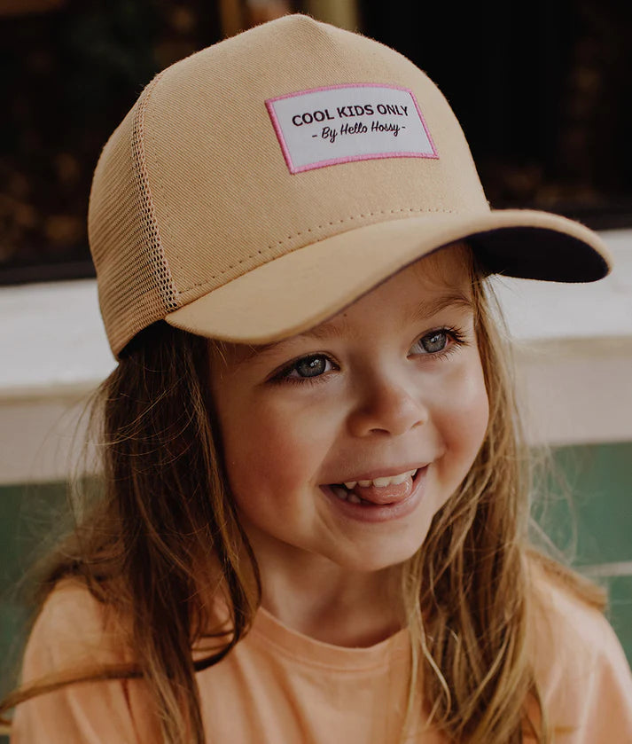 Menina feliz a usar o boné trucker Mini Melba bege da Hello Hossy com etiqueta "Cool Kids Only".