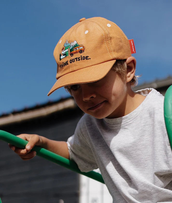 Criança com boné Hello Hossy Outside de linho e algodão a brincar ao ar livre, ideal para proteger do sol.