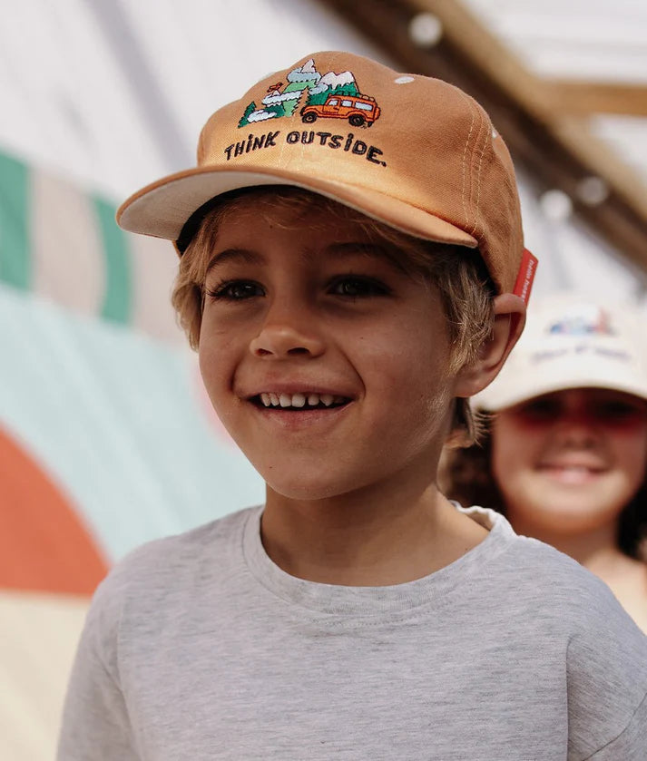 Criança feliz com boné Hello Hossy Outside de linho e algodão, mostrando conforto e design para aventuras.