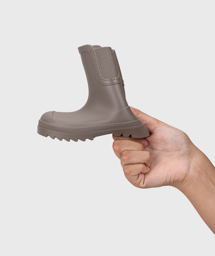 Mão a segurar uma Igor Galochas Verona Taupe, demonstrando a flexibilidade da sola e do cano da galocha.