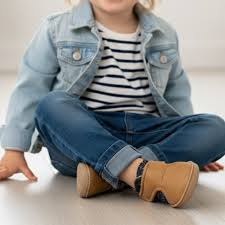 Criança sentada, a usar as sapatilhas Baby Lobitos Barefoot Paulitos Marea em tom castanho com padrão colorido, demonstrando flexibilidade e conforto.