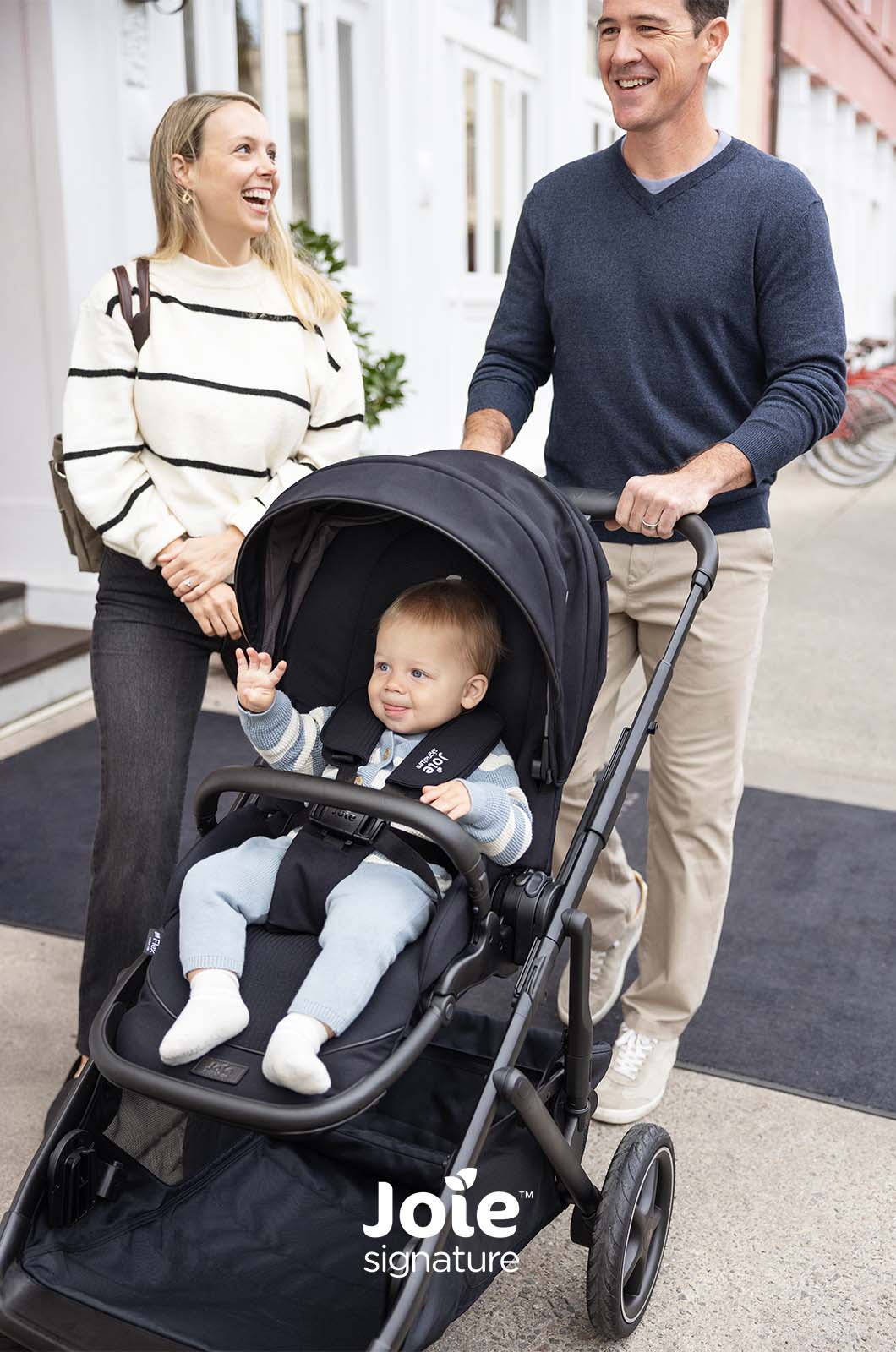 Família (pai e mãe) a passear com bebé num assento do carrinho Joie Versiti Signature.