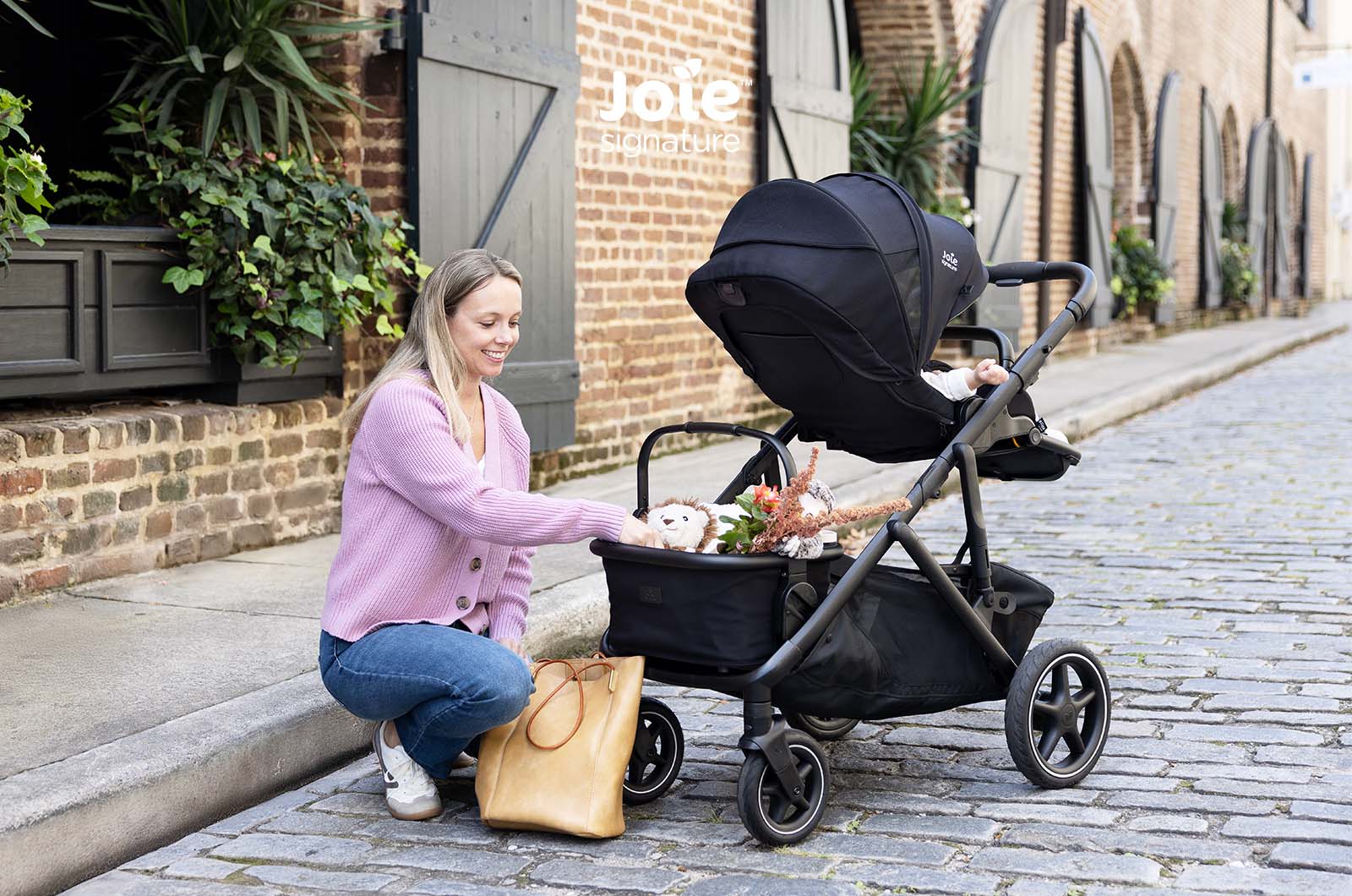 Mãe a colocar brinquedos no cesto do carrinho Joie Versiti Signature.