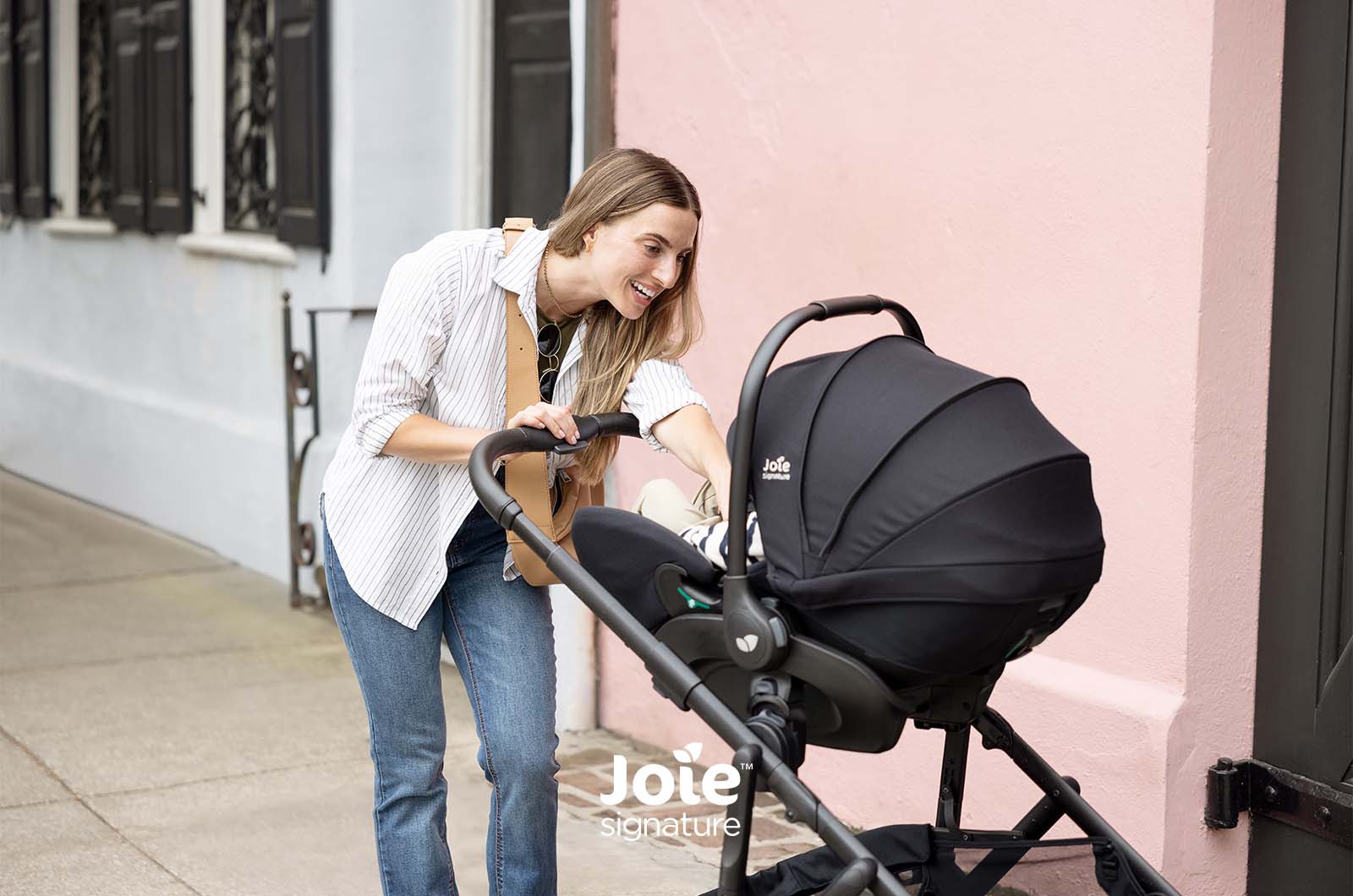 Mãe a colocar cadeira auto Joie no chassis do carrinho Versiti Signature.