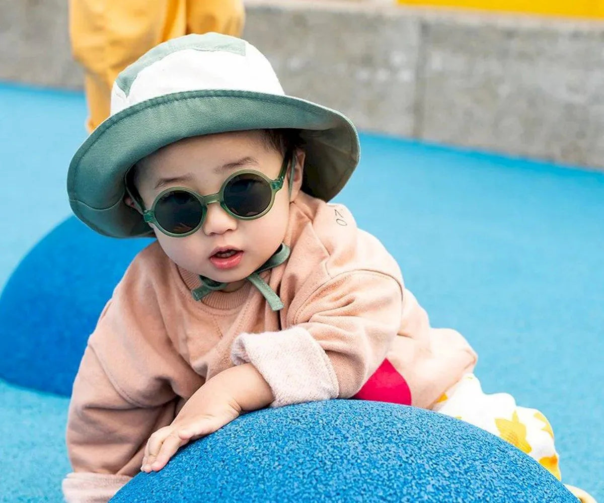 Bebé usando o chapéu Panamá Kietla verde e natural, brincando ao ar livre. Proteção solar UPF 50+ em ação.