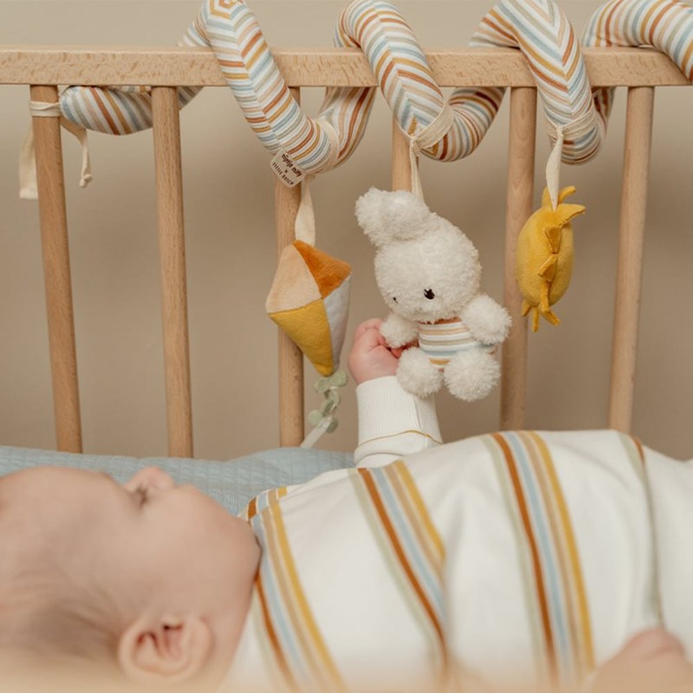 Bebé deitado num berço a tentar alcançar a espiral de atividades Little Dutch Miffy Vintage Stripes pendurada no varão.