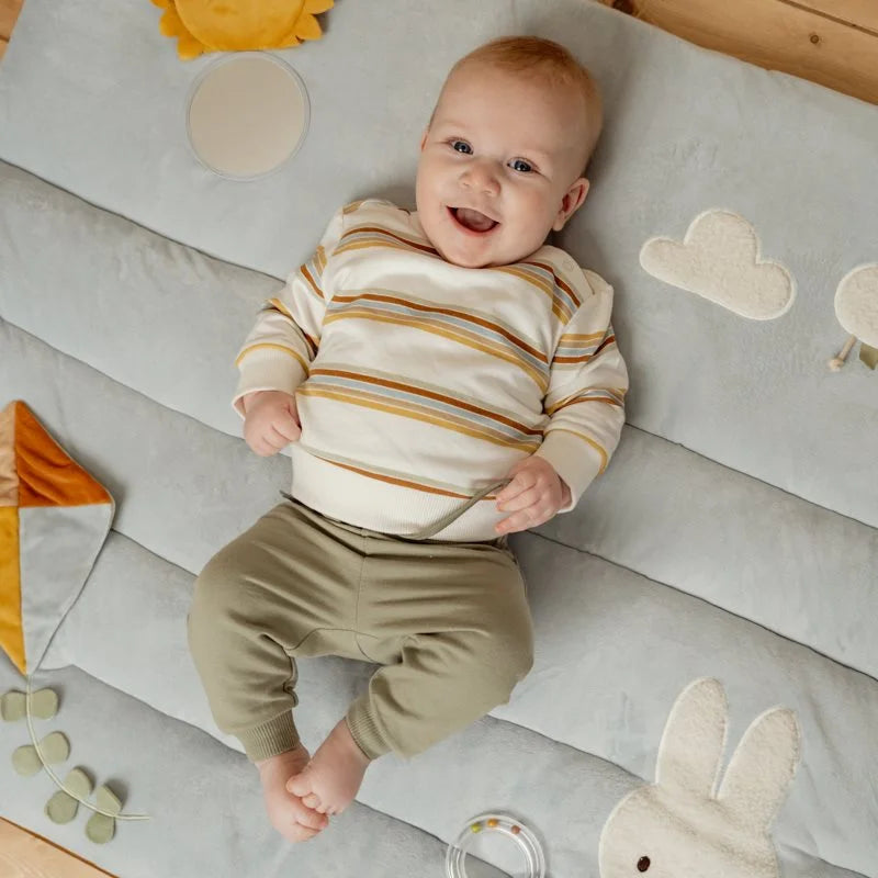Bebé feliz a brincar de barriga para cima no tapete de atividades Little Dutch Sunny Stripes.