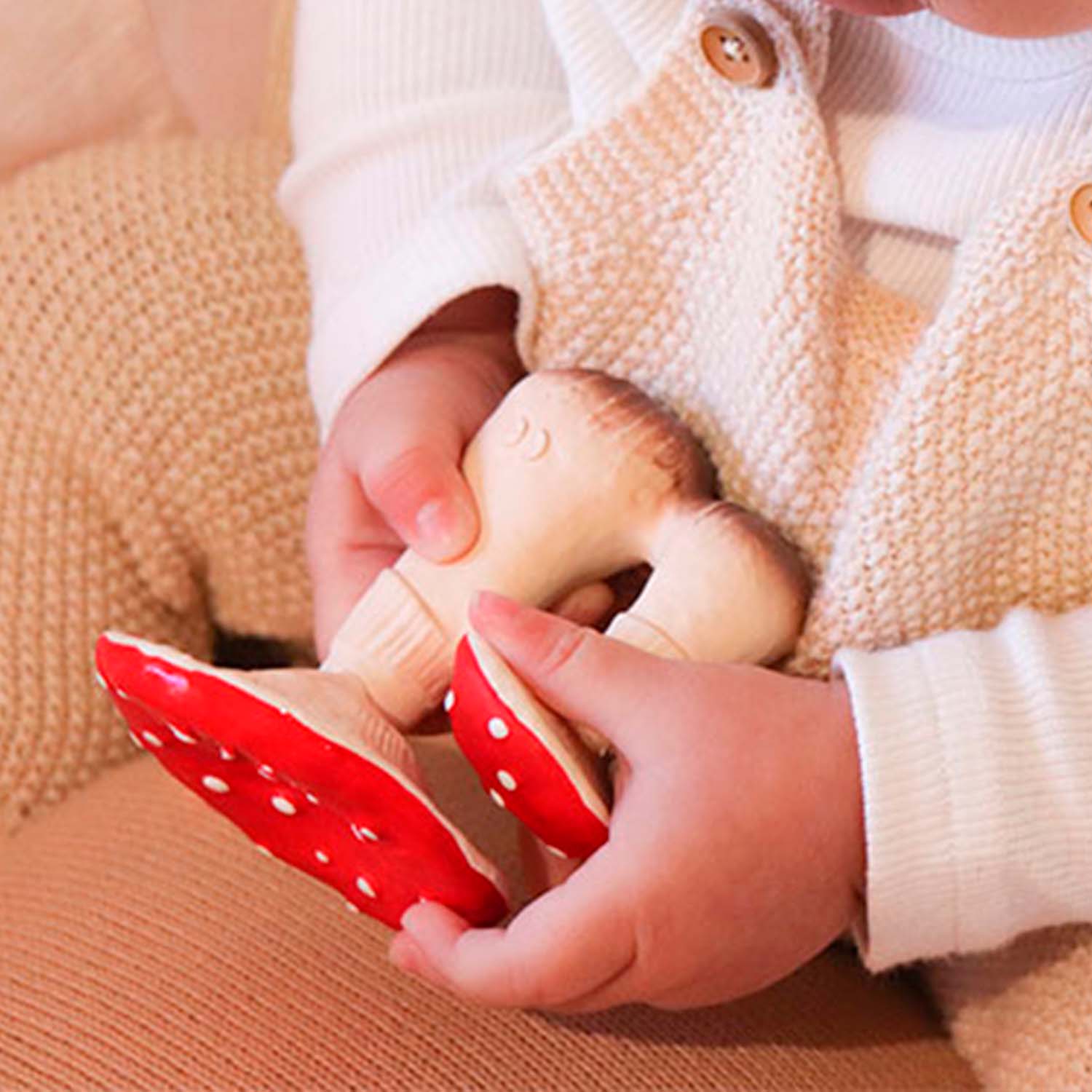 Mãos de um bebé a segurar o mordedor Spot o Cogumelo, mostrando o tamanho e a forma ergonómica do brinquedo.