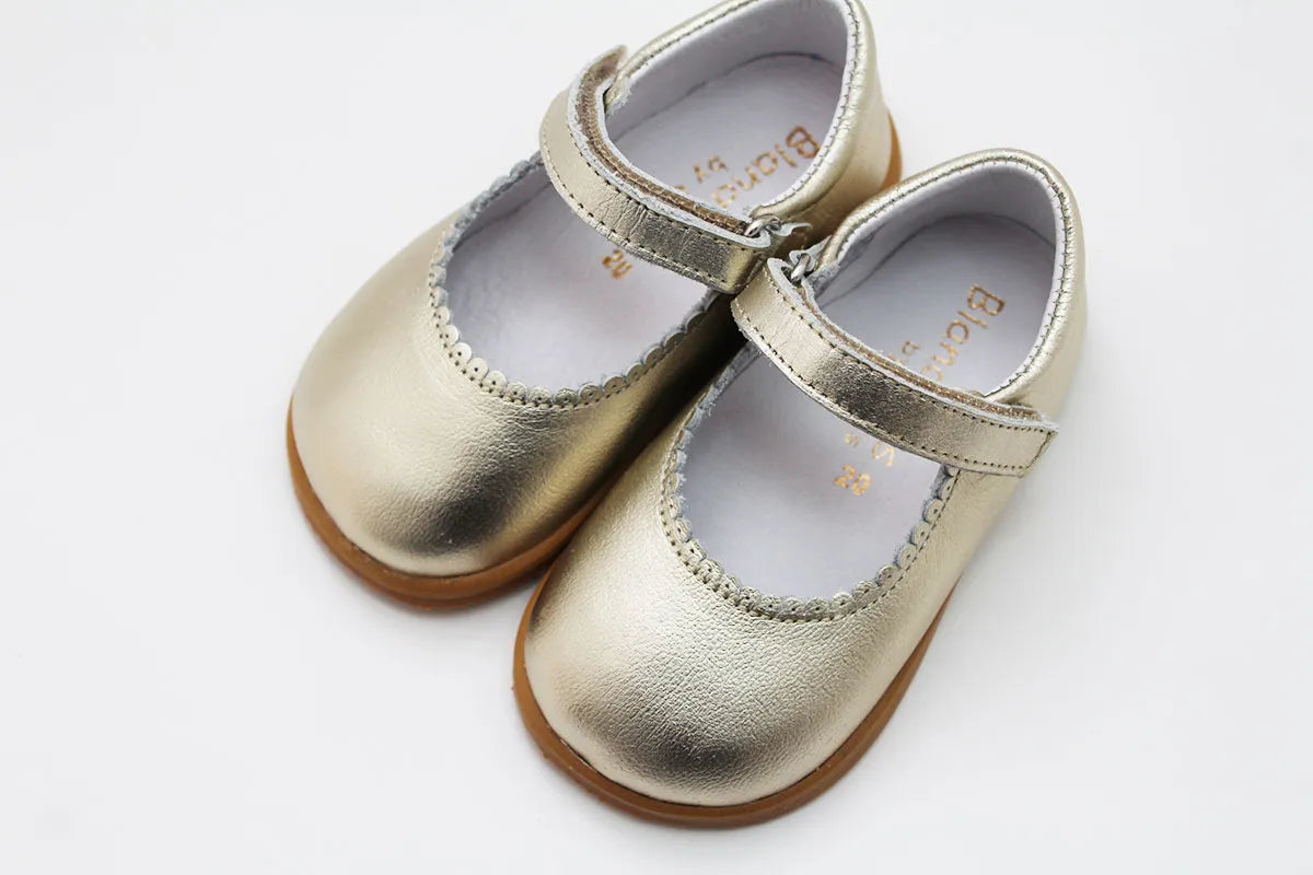 Vista superior de um par de Merceditas Chloe em pele cor champagne, com fecho em Velcro e detalhes em pele macia.