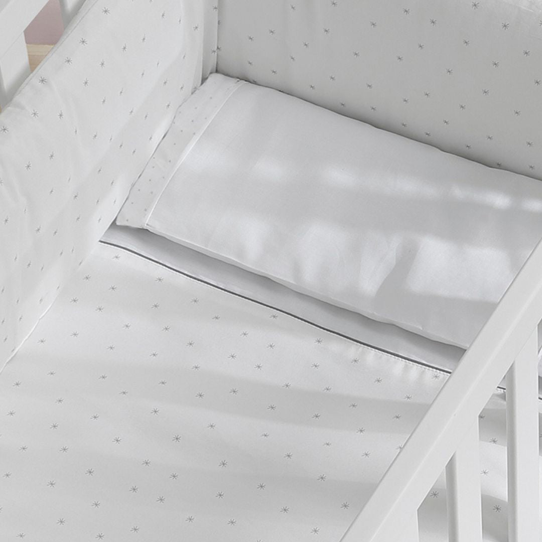 Detalhe do Kit Micuna nórdico e protector para minicuna em branco, com padrão de estrelas cinzentas e almofada.