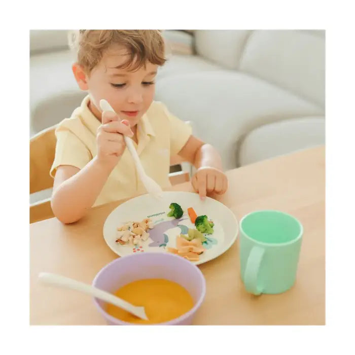 Criança a usar o garfo do conjunto Miniland Dream para comer do prato de unicórnio, com sopa na tigela.