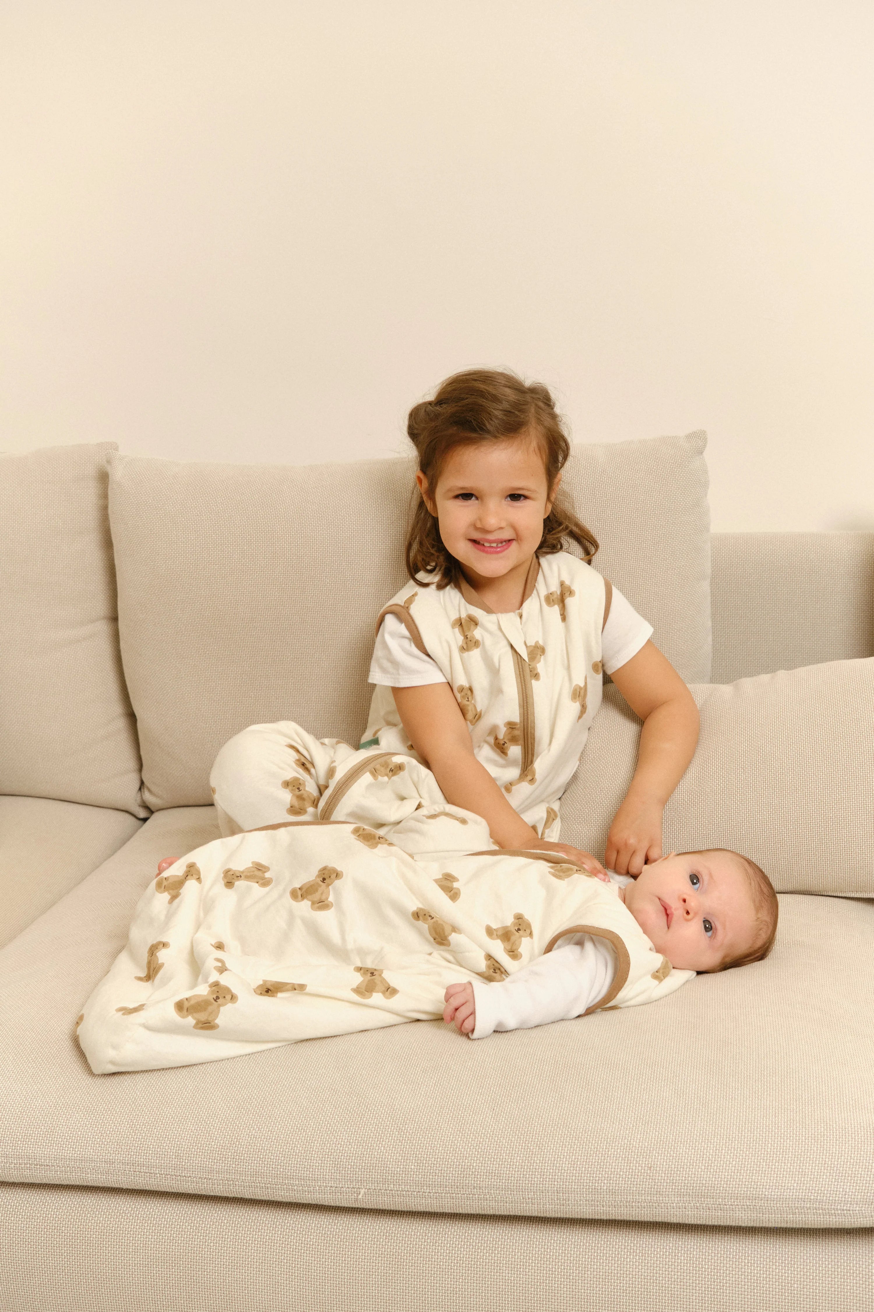 Bebé em saco de dormir MolisandCo TOG 1.0 Teddy creme, deitado no sofá com criança sorridente. Conforto e estilo.