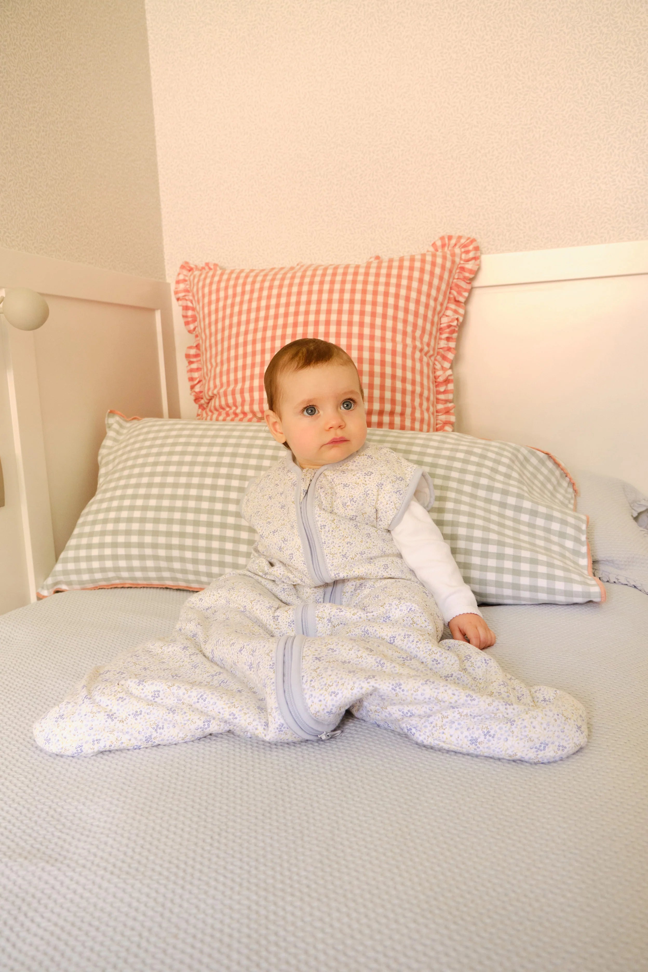 Bebé sentado na cama, a usar o saco de dormir MolisandCo TOG 1.0 Blue Lily, mostrando liberdade de movimentos.