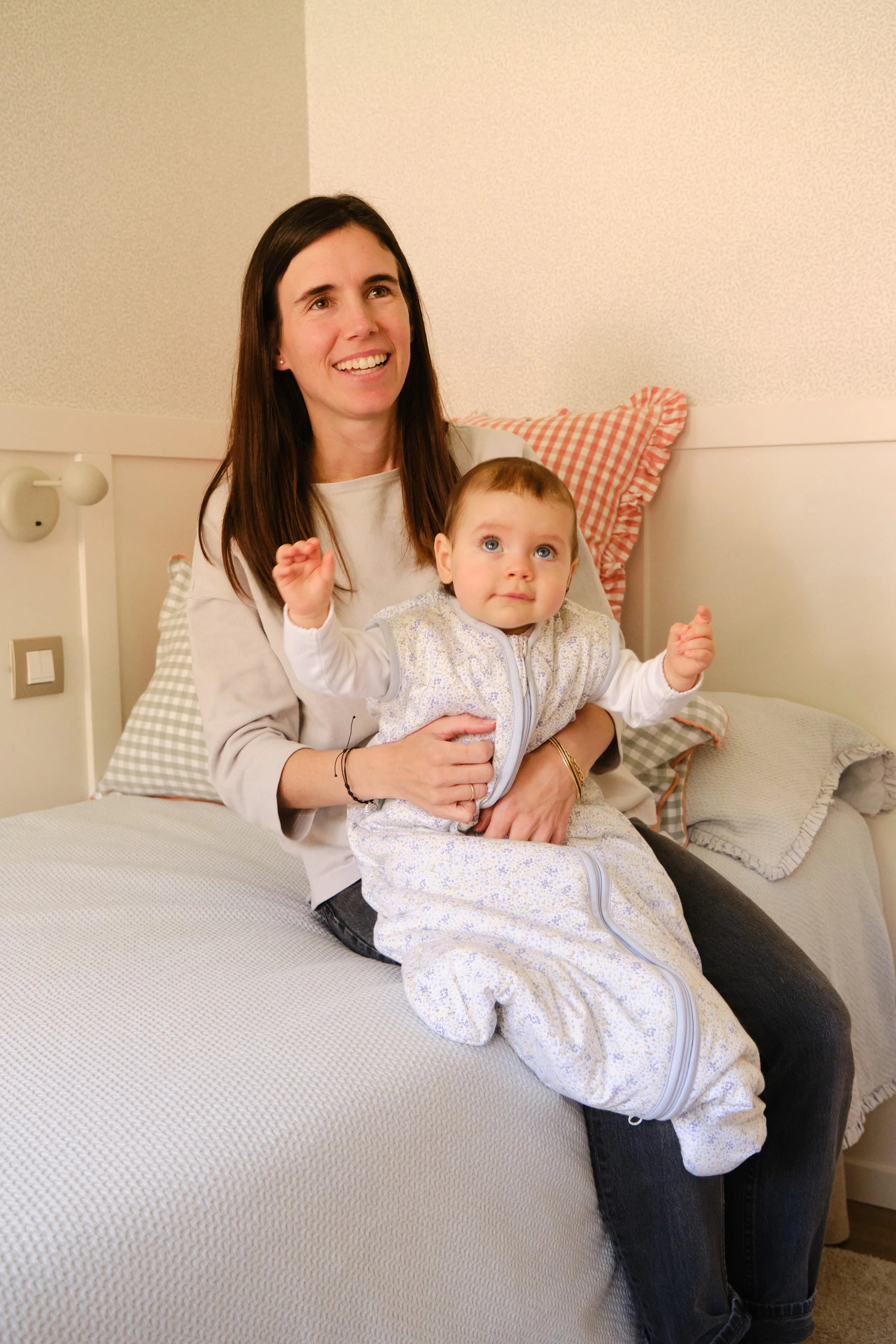 Mãe a segurar bebé feliz com saco de dormir MolisandCo TOG 1.0 Blue Lily no colo, momento de carinho.