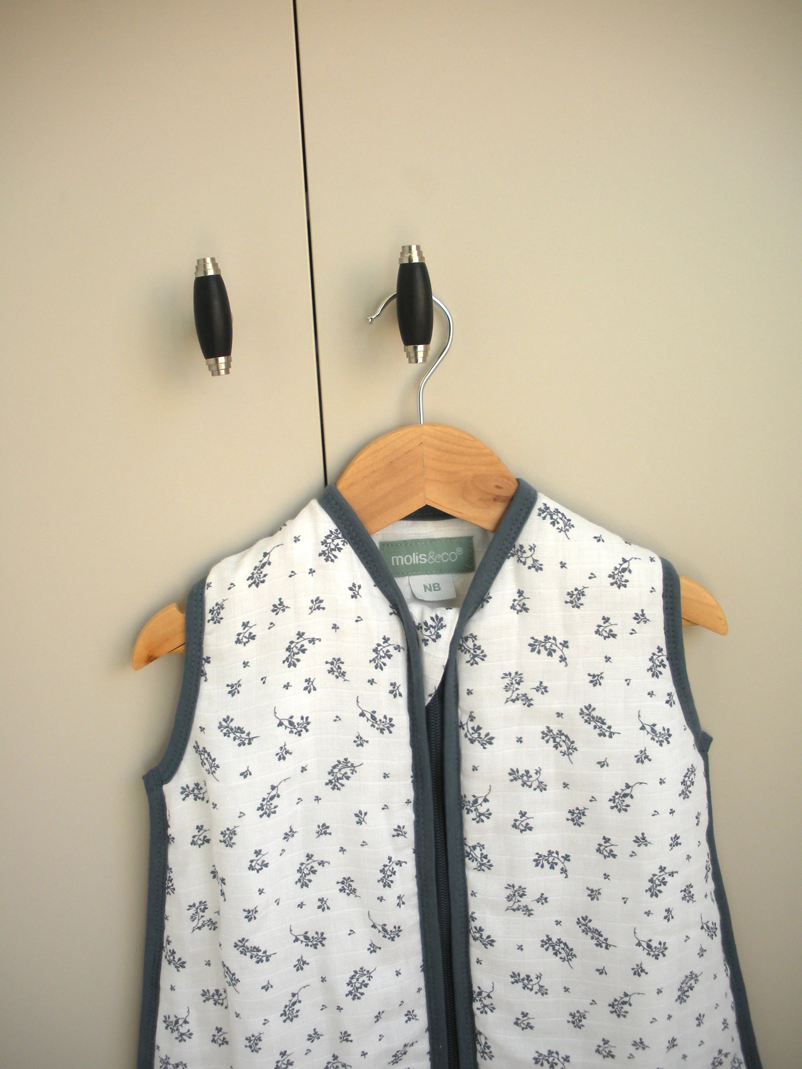 Detalhe do saco de dormir MolisandCo TOG 1.0, algodão musselina, padrão floral, pendurado, etiqueta visível.