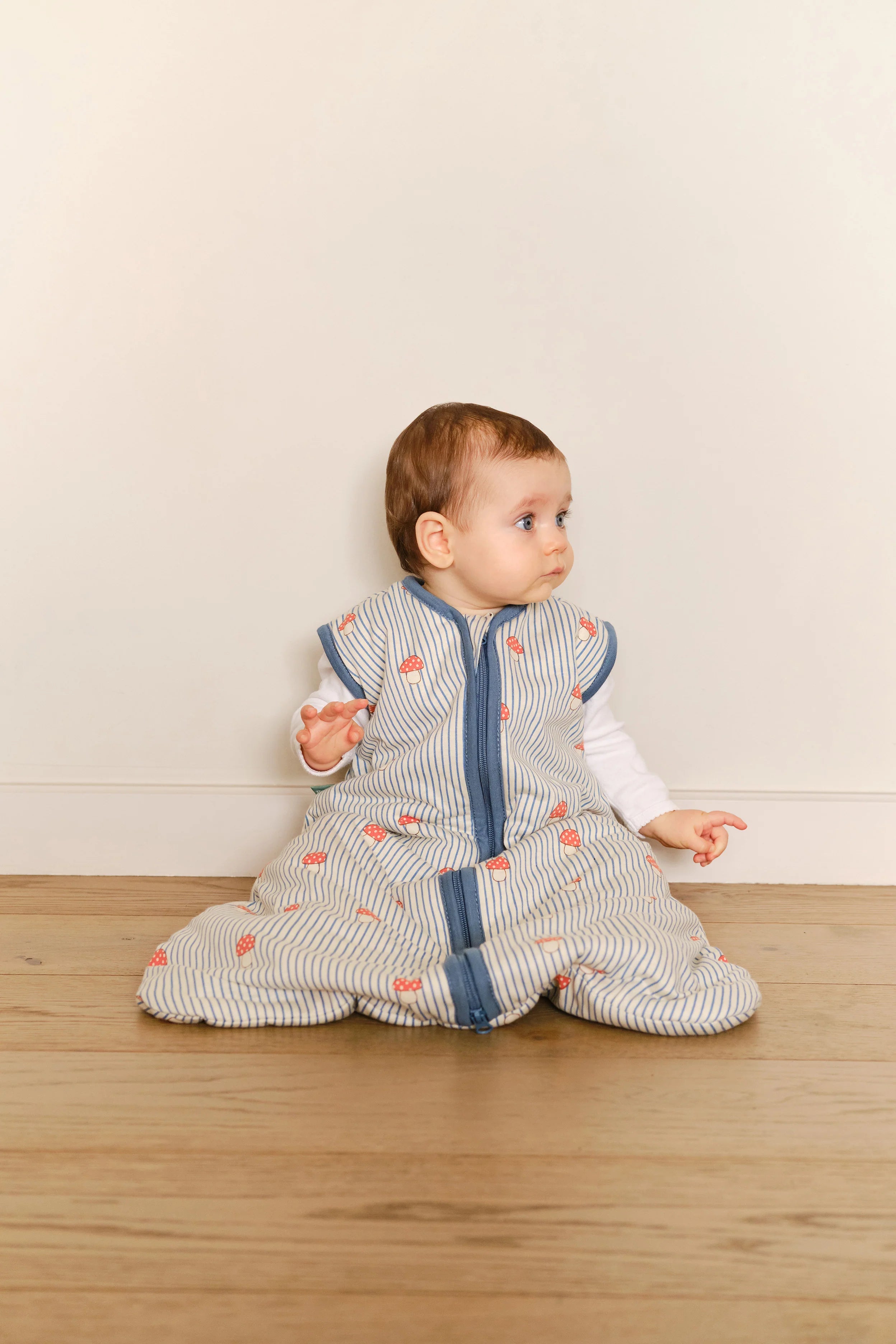 Bebé sentado no chão, a usar saco de dormir MolisandCo TOG 1.0 'Mushrooms', com total liberdade de movimento.