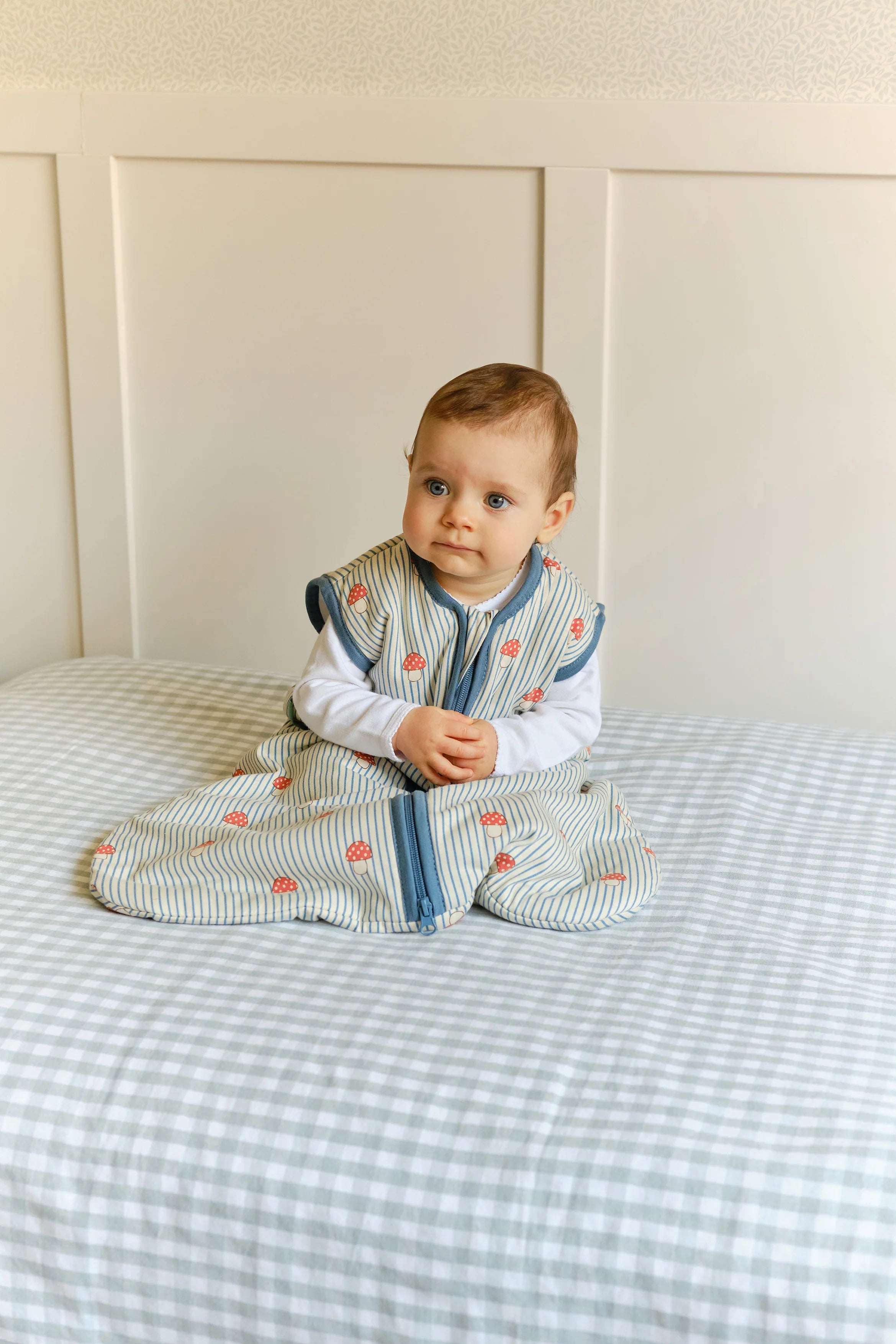 Bebé sentado na cama, a usar saco de dormir MolisandCo TOG 1.0 'Mushrooms', mostrando liberdade de movimento.