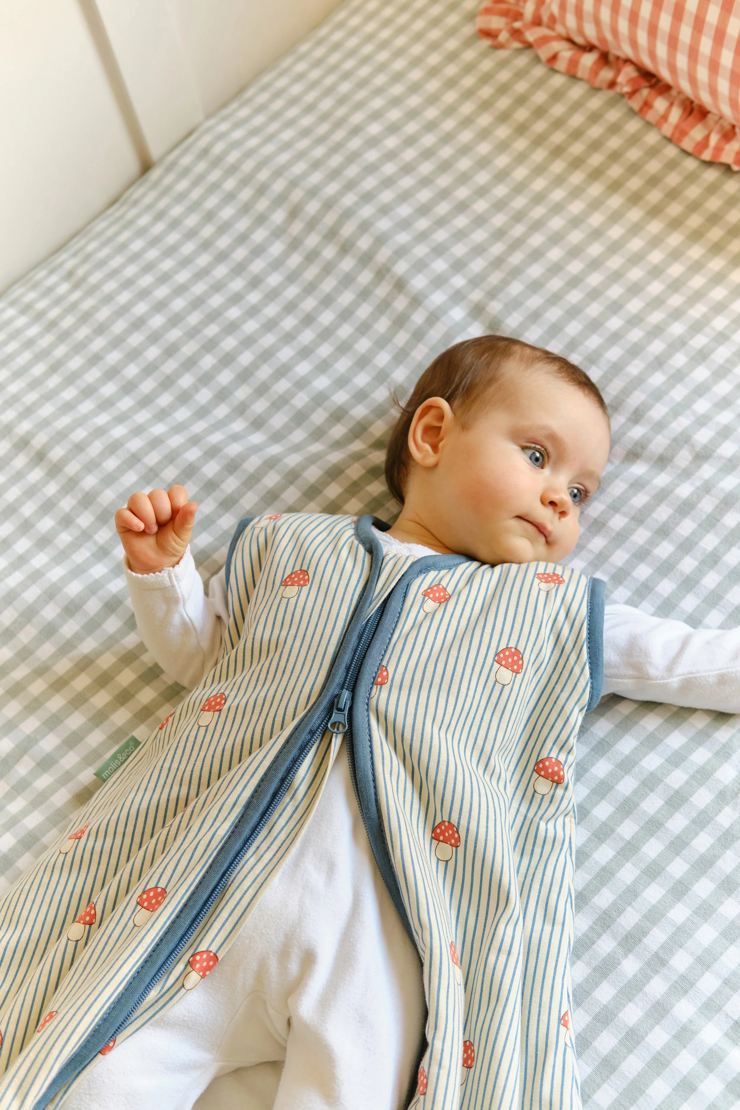 Close-up de bebé feliz deitado no saco de dormir MolisandCo TOG 1.0 'Mushrooms', destacando o padrão.