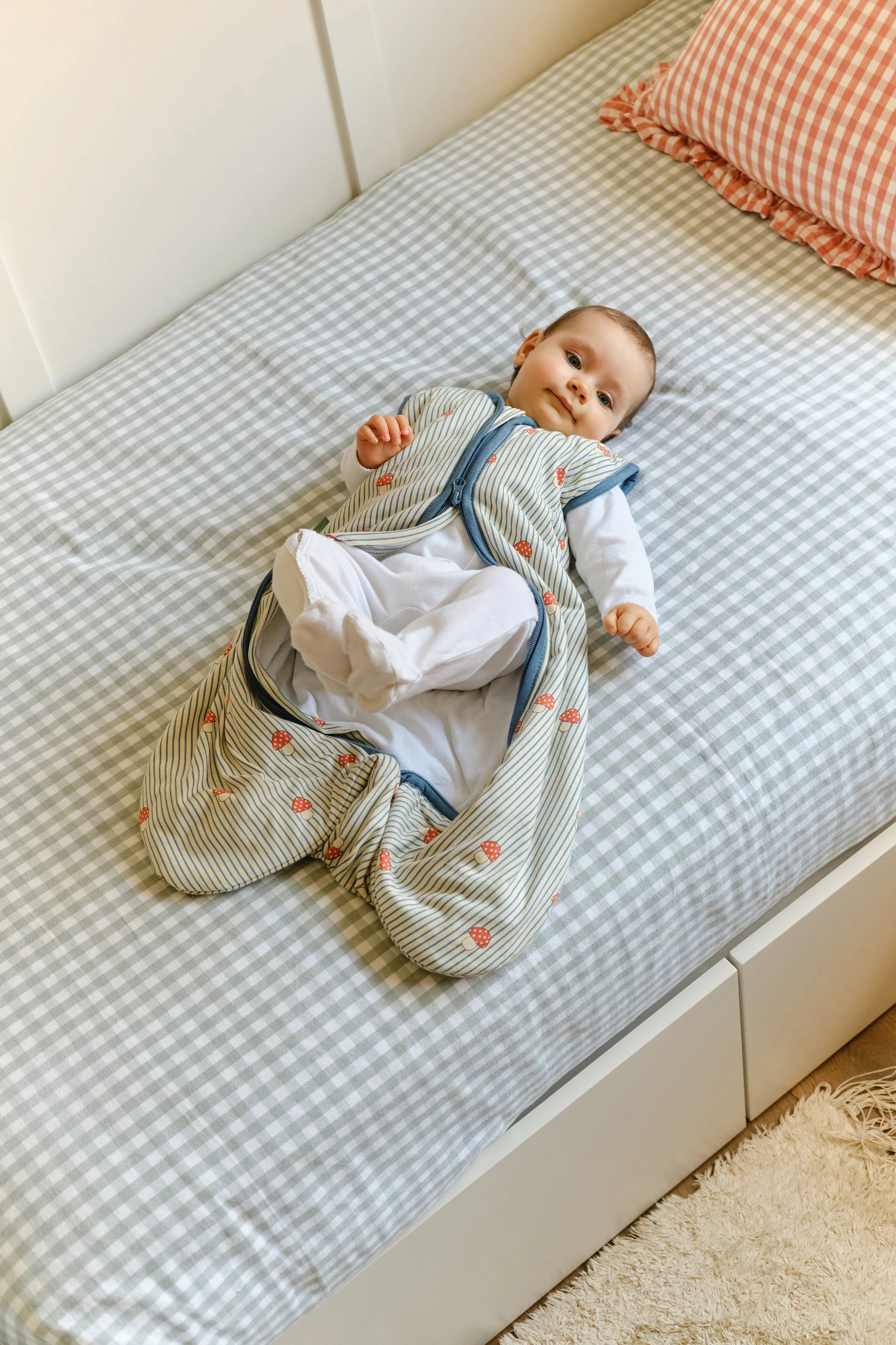 Bebé deitado mostra liberdade de movimento das pernas no saco de dormir MolisandCo TOG 1.0 'Mushrooms' sem pés.
