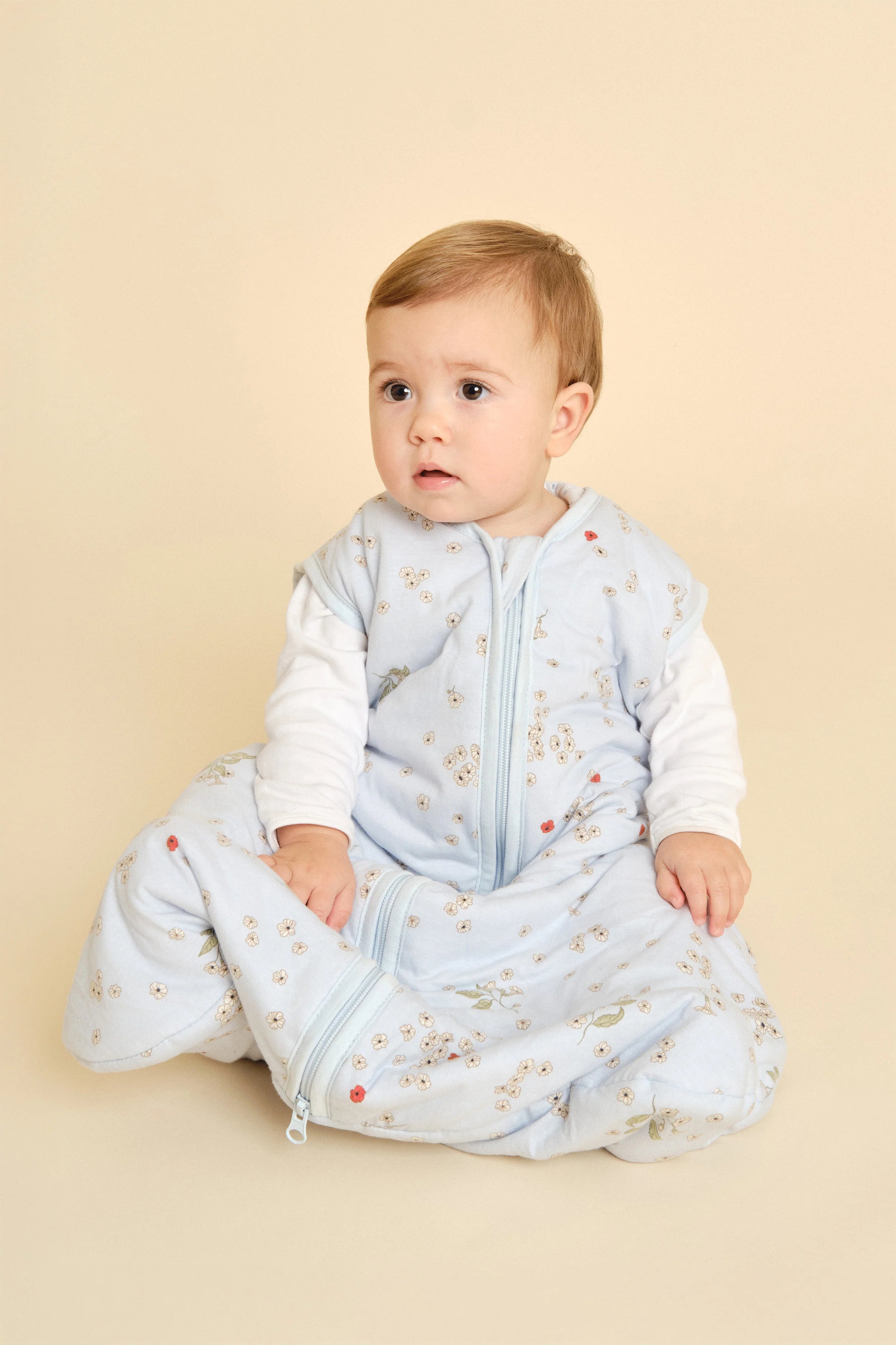 Bebé sentado a usar saco de dormir MolisandCo TOG 1.0 "Poppy" azul. Destaca a liberdade de movimento e conforto.