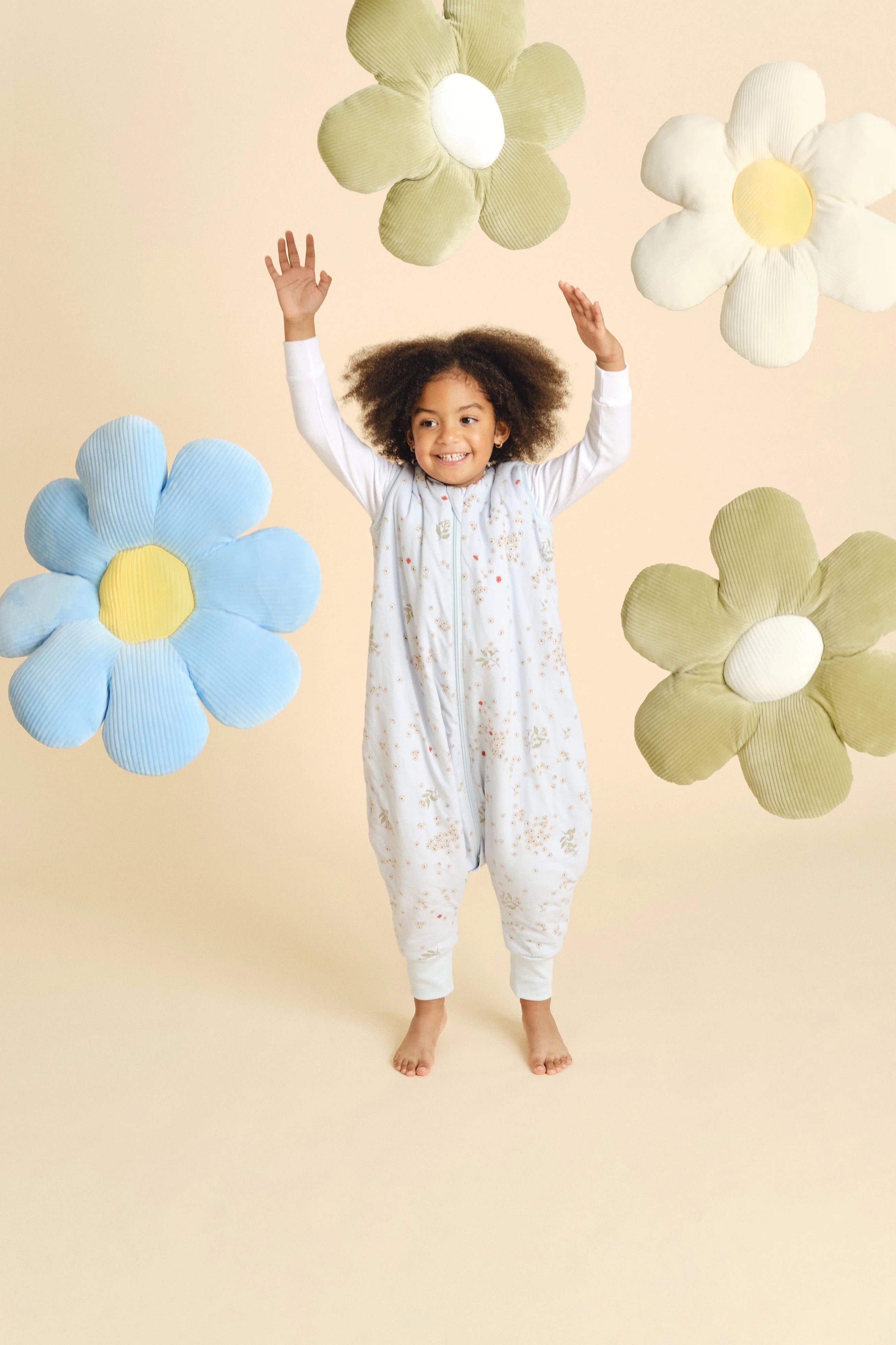 Criança feliz, braços erguidos, a brincar com flores, usando saco de dormir MolisandCo TOG 1.0 Poppy.
