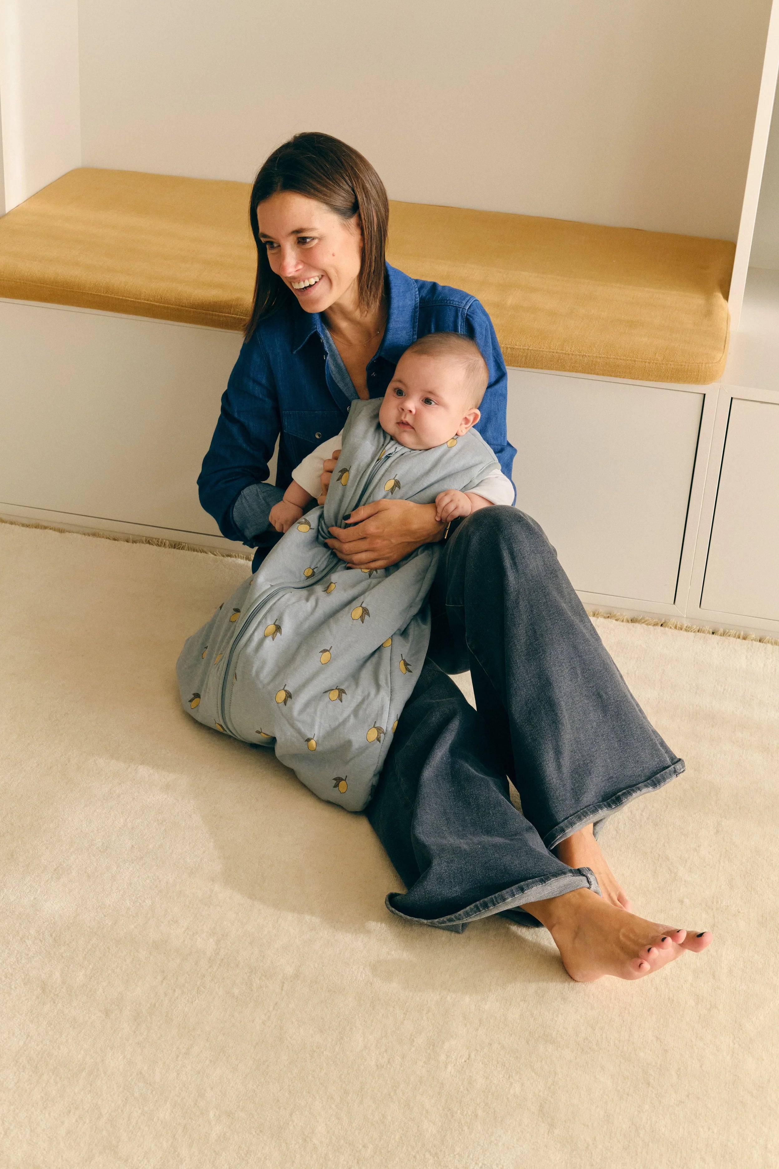 Mãe sorridente segura bebé aconchegado no saco de dormir MolisandCo Colima, azul com limões. Conforto e segurança.
