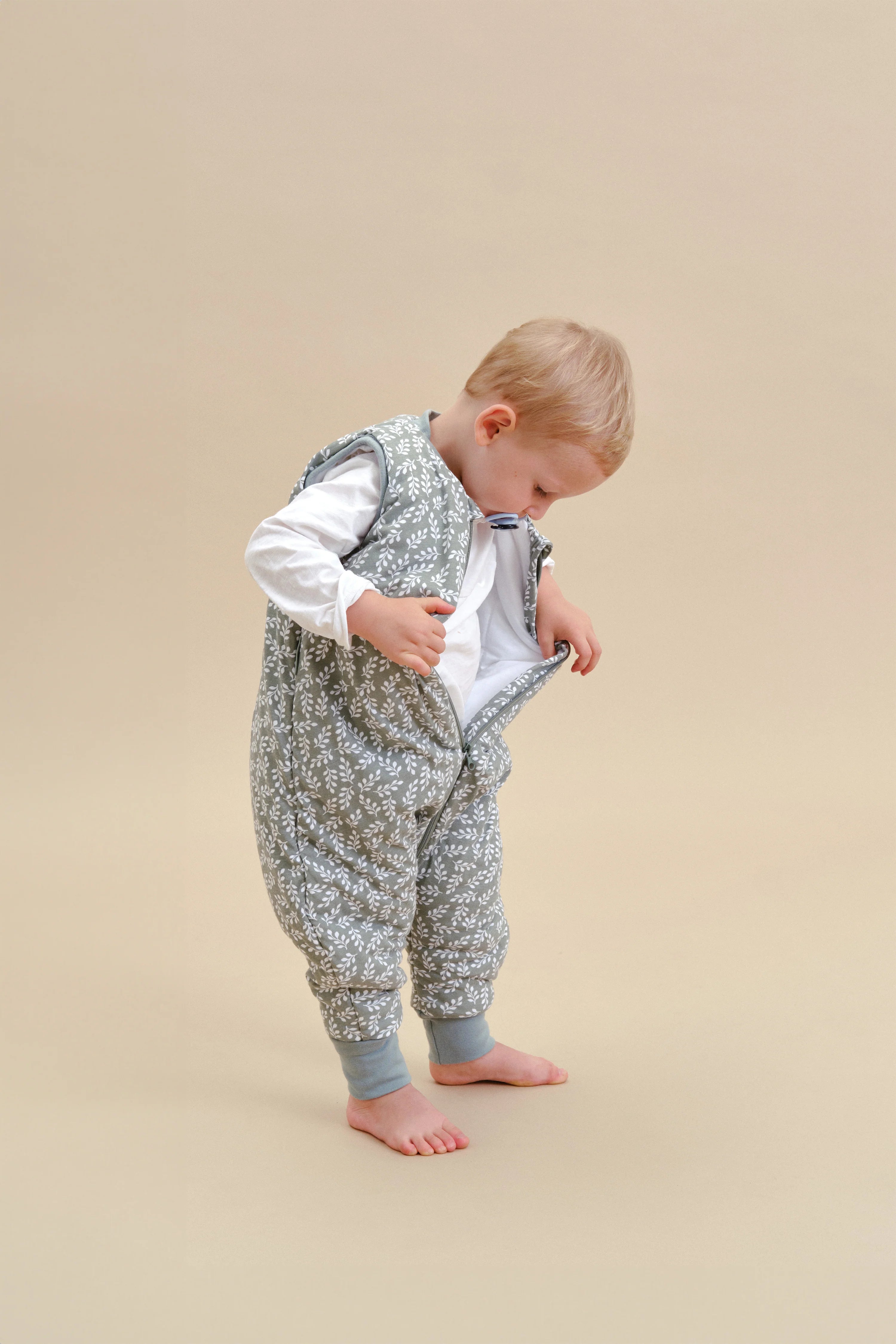 Bebé loiro com saco de dormir MolisandCo Green Garden, a interagir com o fecho frontal. Conforto e praticidade.