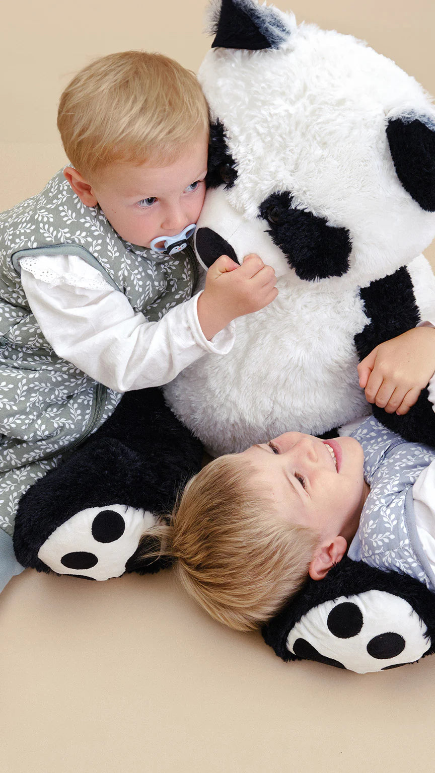 Duas crianças com sacos de dormir MolisandCo Green Garden a brincar com um panda de peluche gigante.
