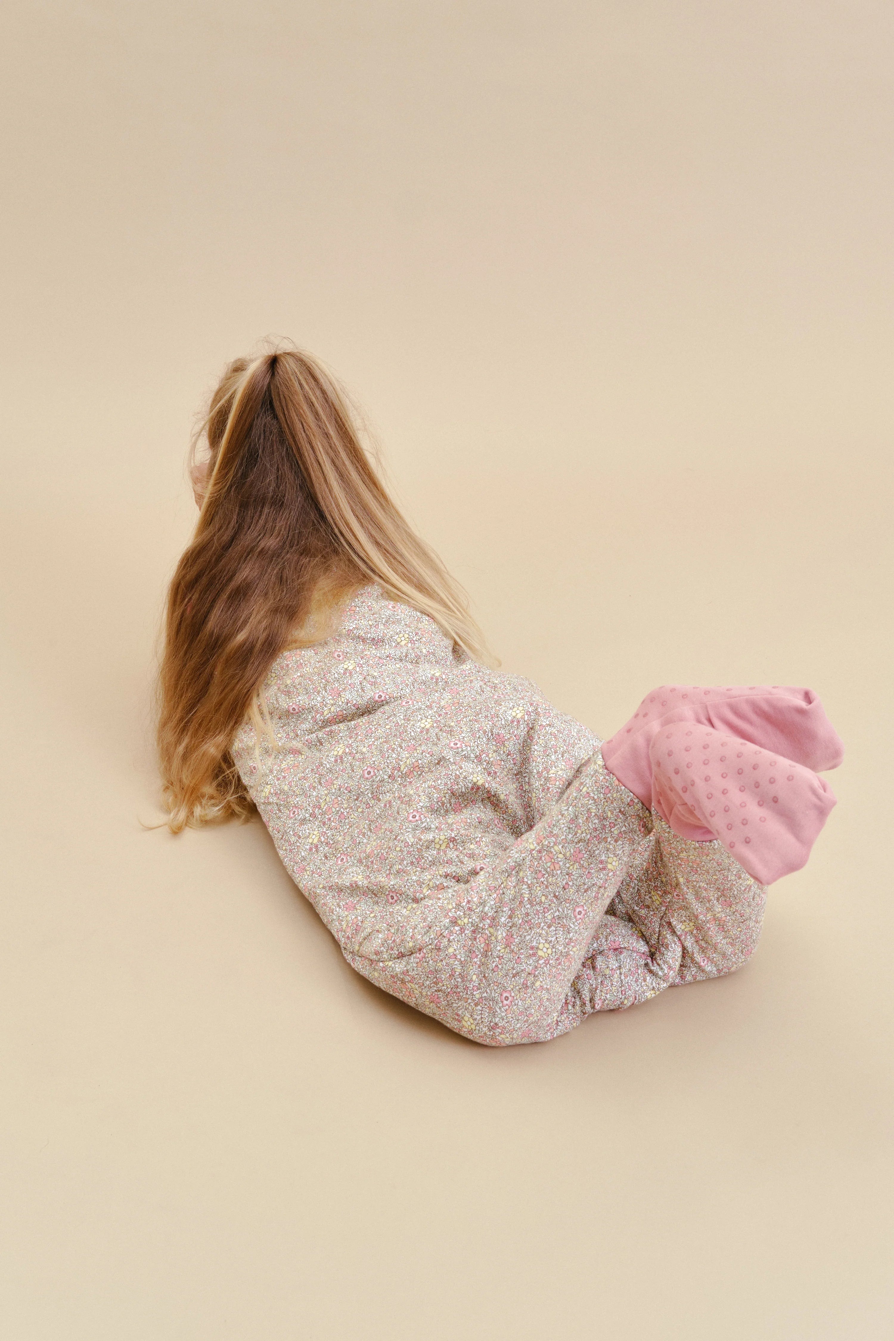 Criança deitada, com saco de dormir MolisandCo TOG 2.5 Pastel Floral e meias antiderrapantes.