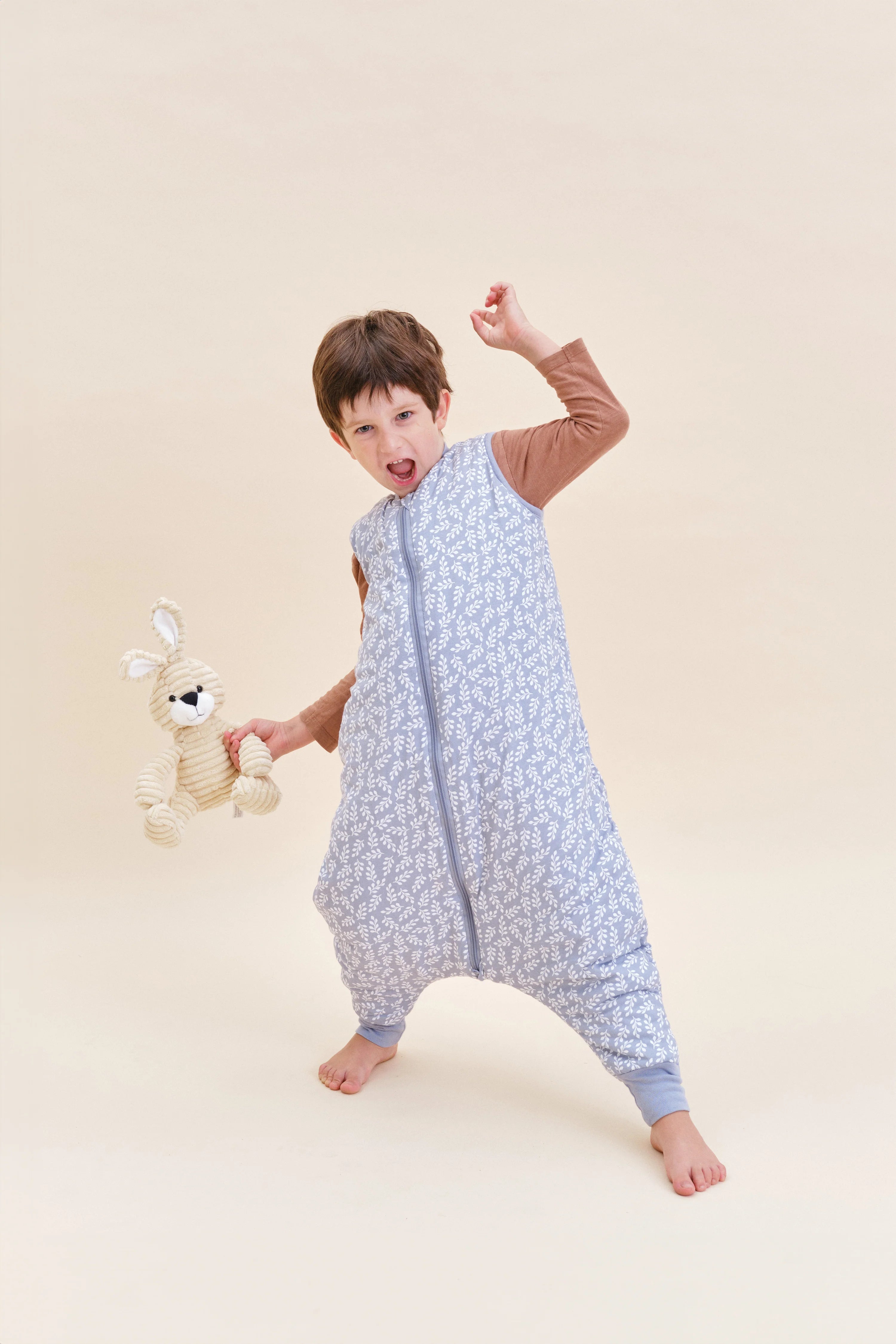 Criança feliz e ativa com saco de dormir MolisandCo TOG 2.5 Blue Garden e brinquedo de coelho.