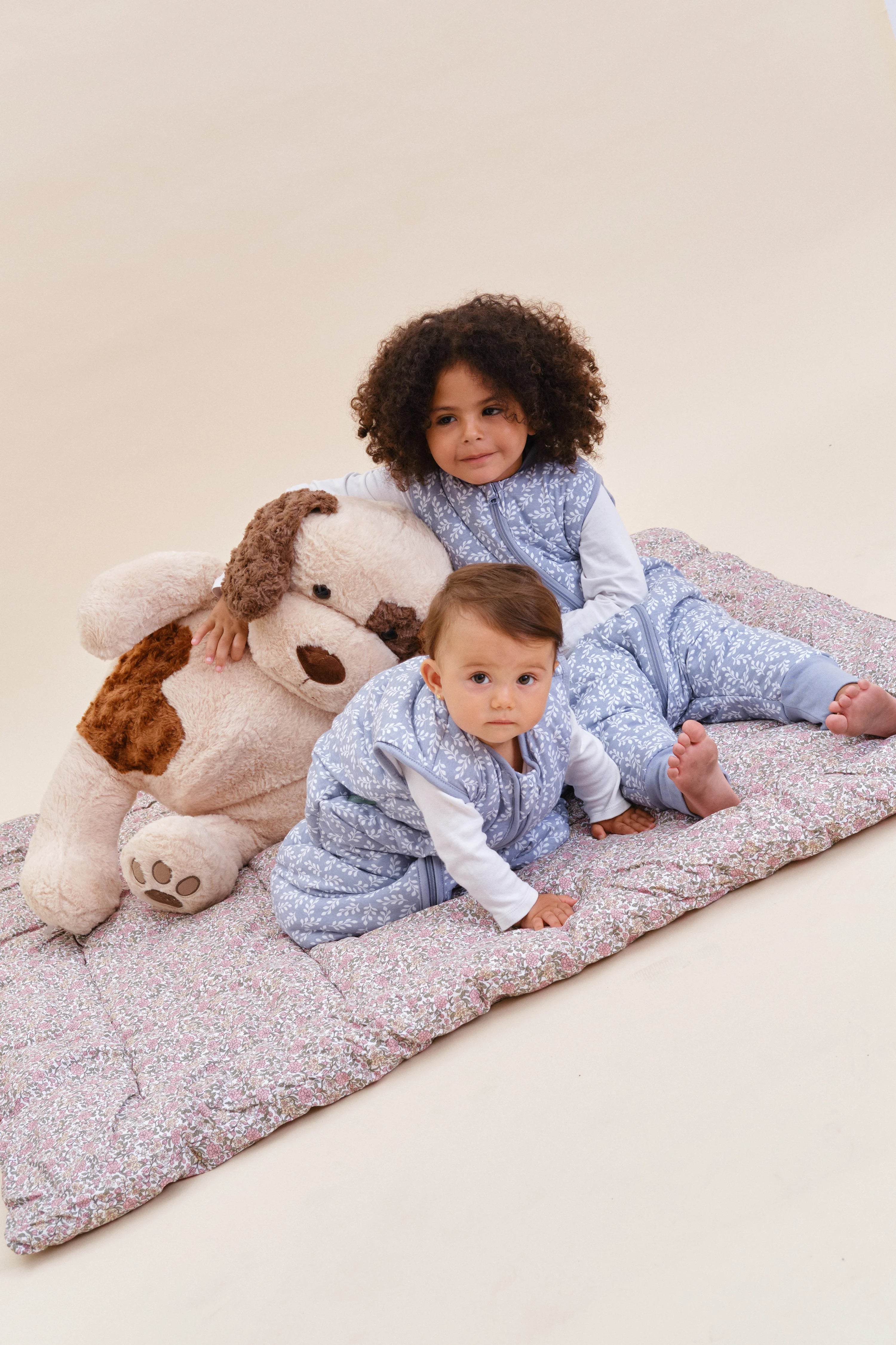 Dois bebés com sacos de dormir MolisandCo TOG 2.5 Blue Garden, deitados com um peluche de cão.