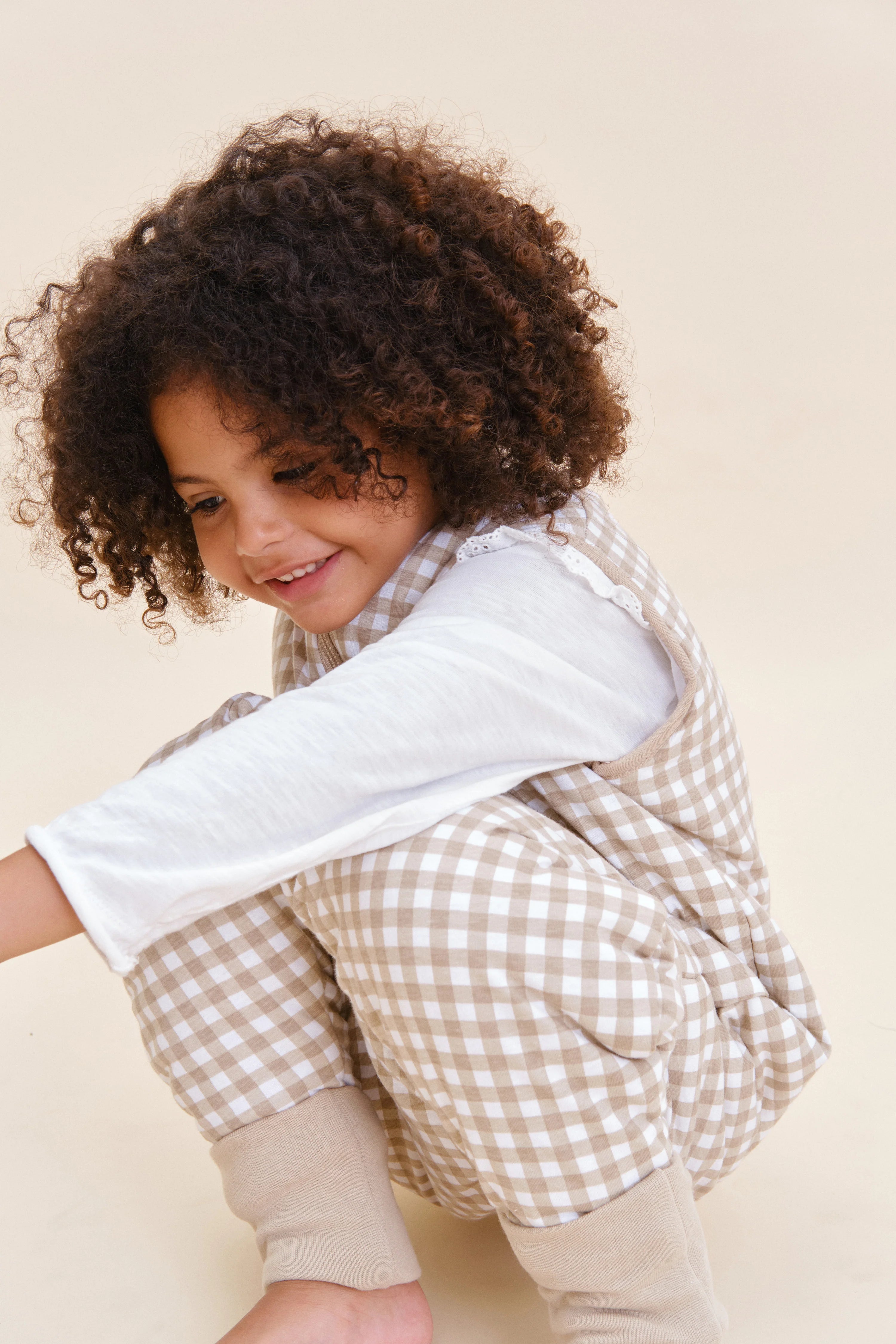 Criança feliz agachada com saco de dormir MolisandCo TOG 2.5 Vichy Bege, detalhe do tecido e pés.